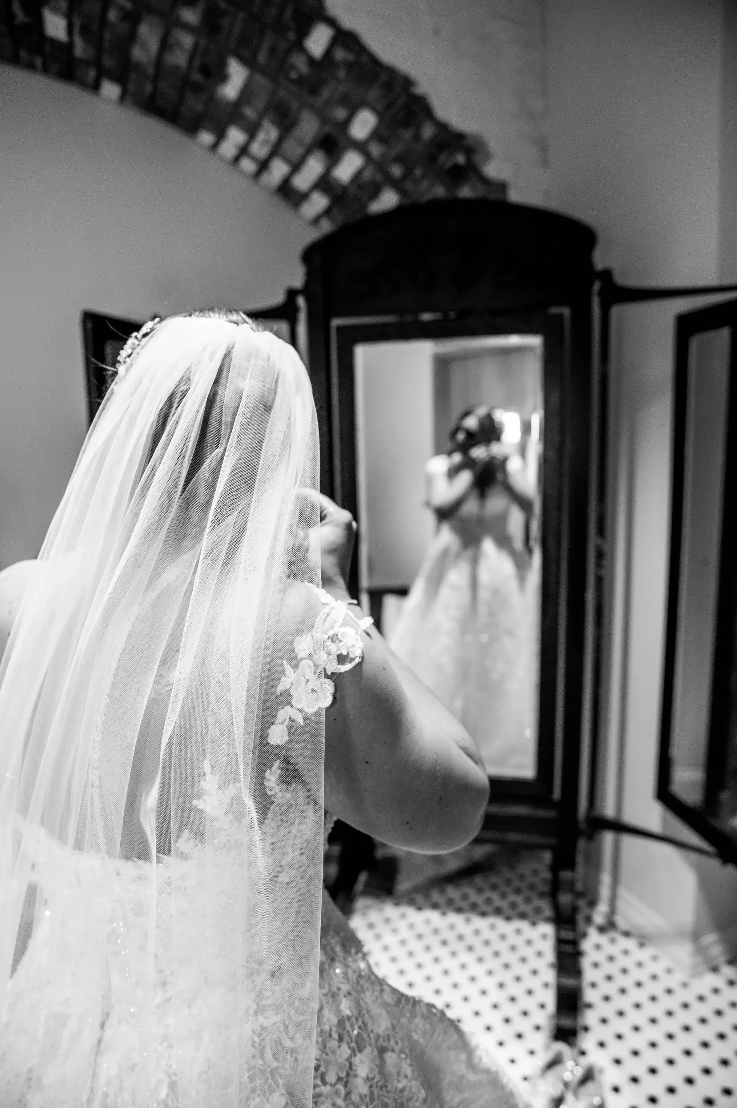 Bride in wedding dress and veil looking at her reflection in a mirror.