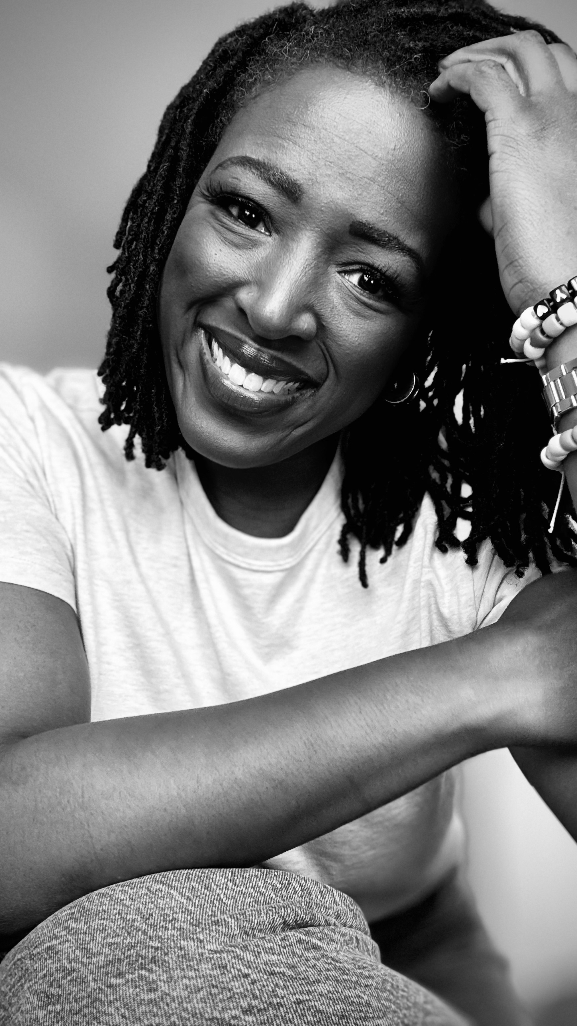 Black and white close-up portrait of a woman with dreadlocks, smiling, wearing a white t-shirt, and looking directly at the camera. Sophia Fifner Keynote Speaker