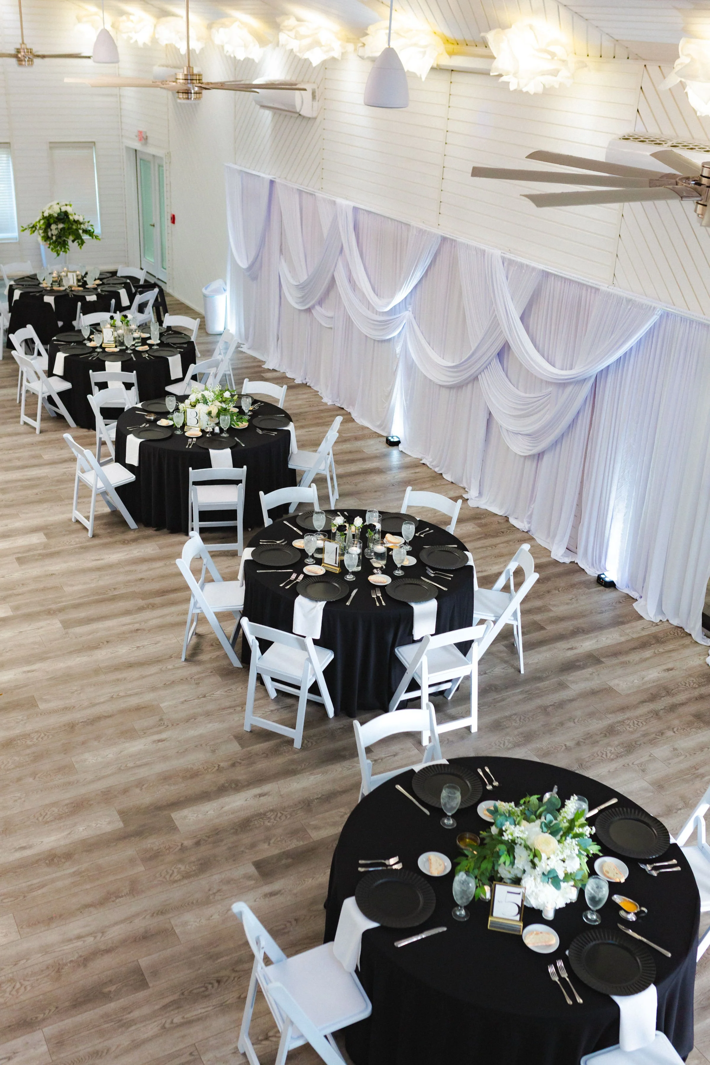 White Indoor Wedding Reception Space with Soft Curtains and Black Tables