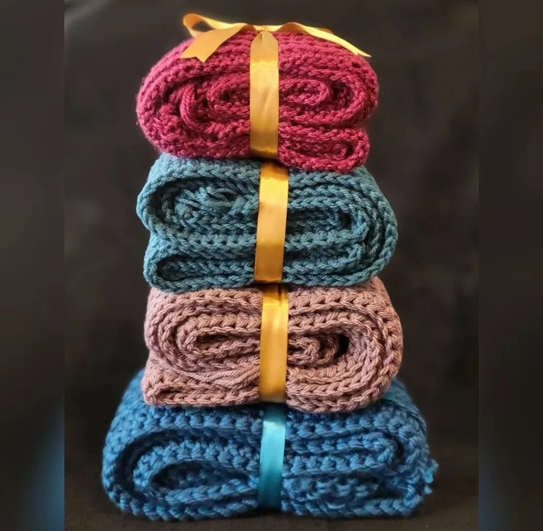 Stacked sets of colorful knit scarves tied with satin ribbons against a dark background.