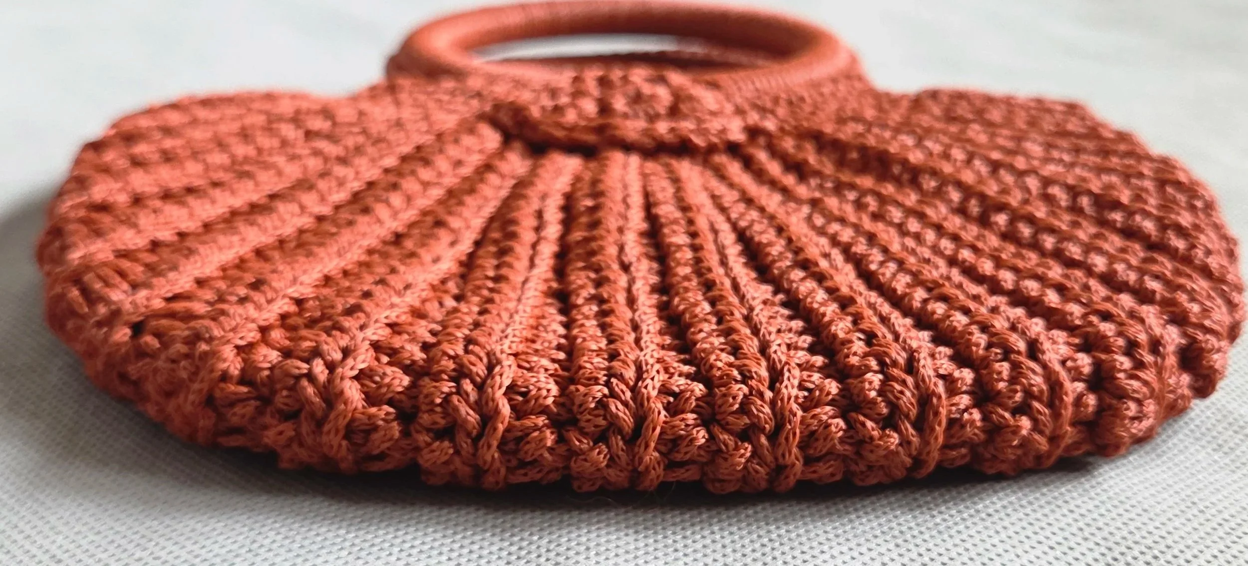 A close-up of a rust-colored, knitted beanie hat with a bow on top, resting on a white textured surface.