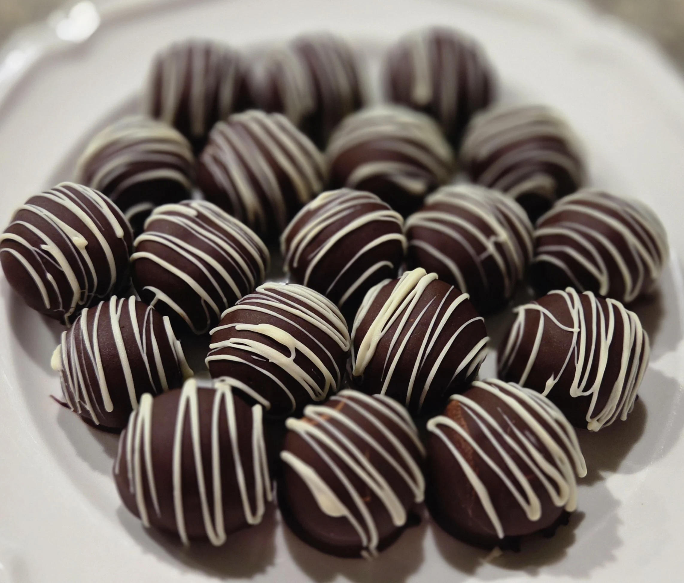 Chocolate truffles decorated with white chocolate drizzle arranged on a white plate.
