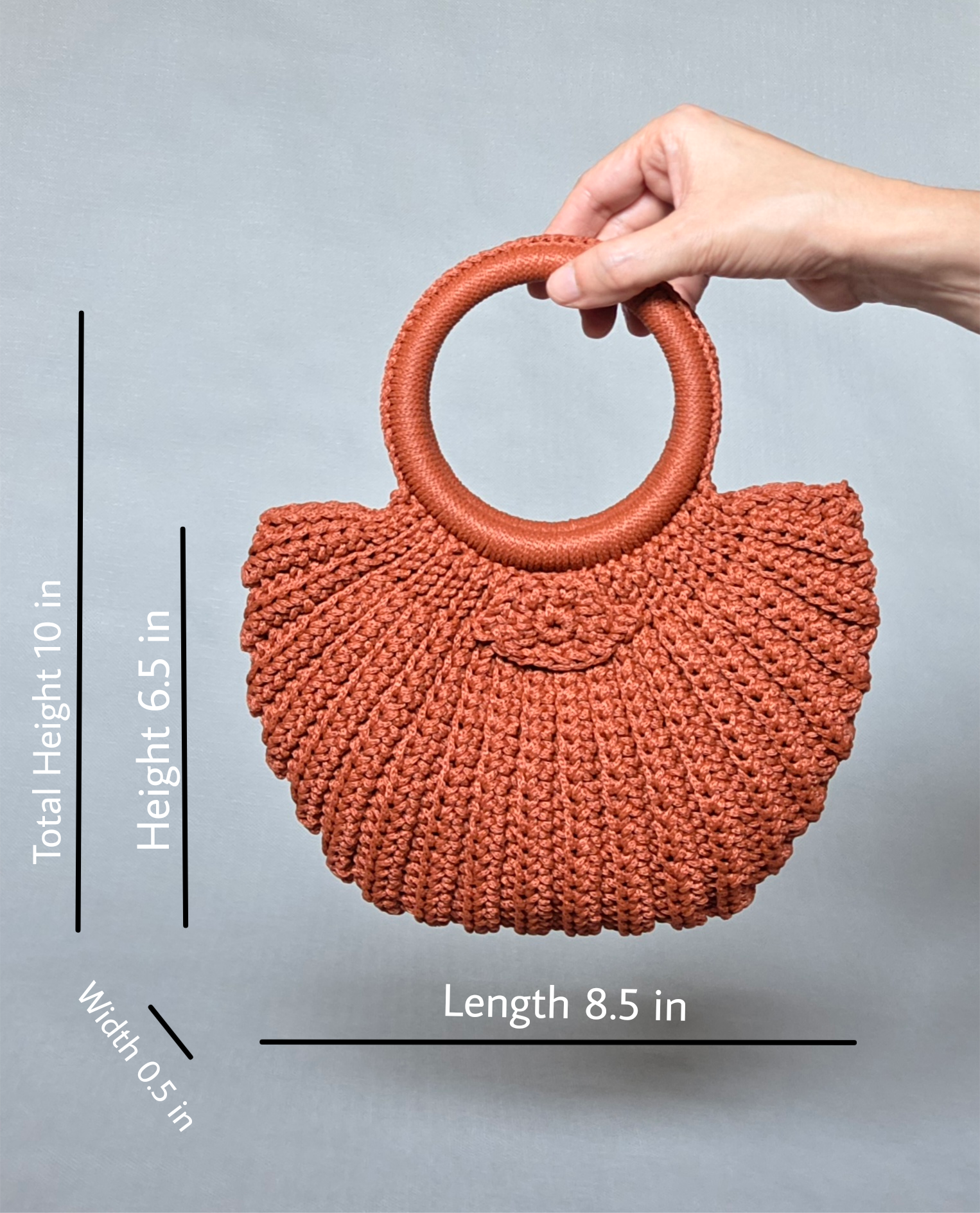 A coral-colored woven handbag with a round handle being held by a person's hand against a plain light gray background.