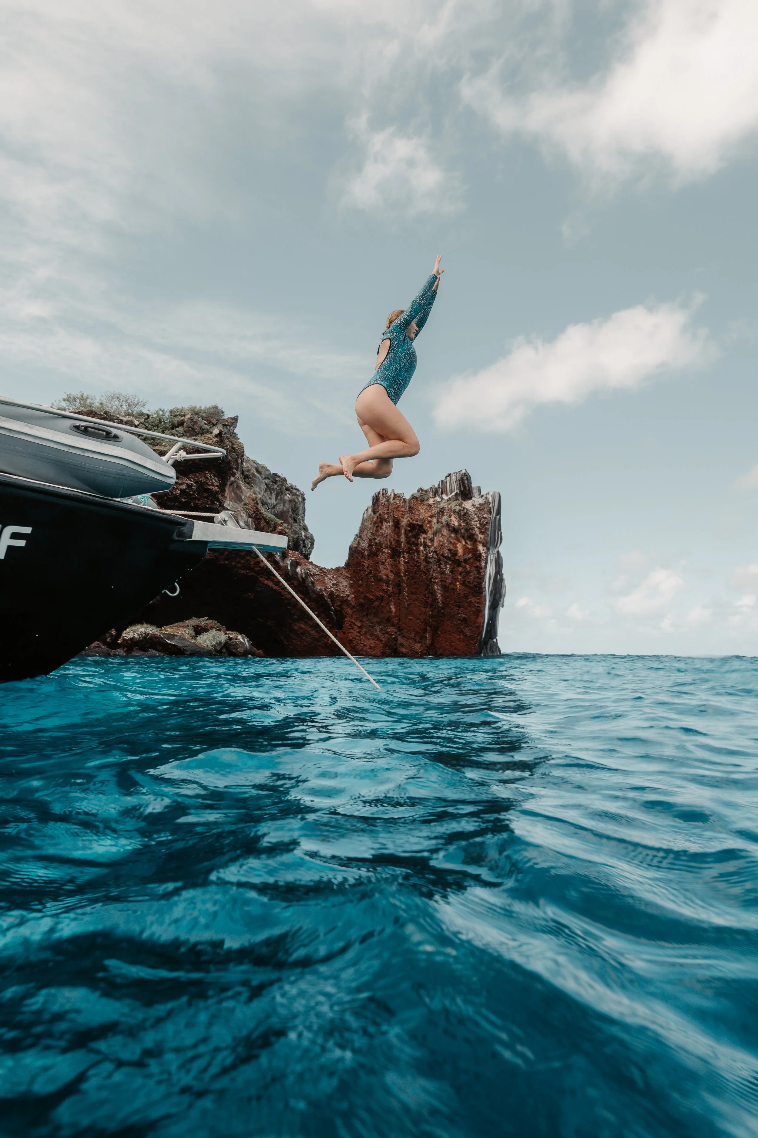 A woman jumping from a boat into the water near a rocky cliff on a sunny day. Galápagos freediving expedition San Cristóbal.