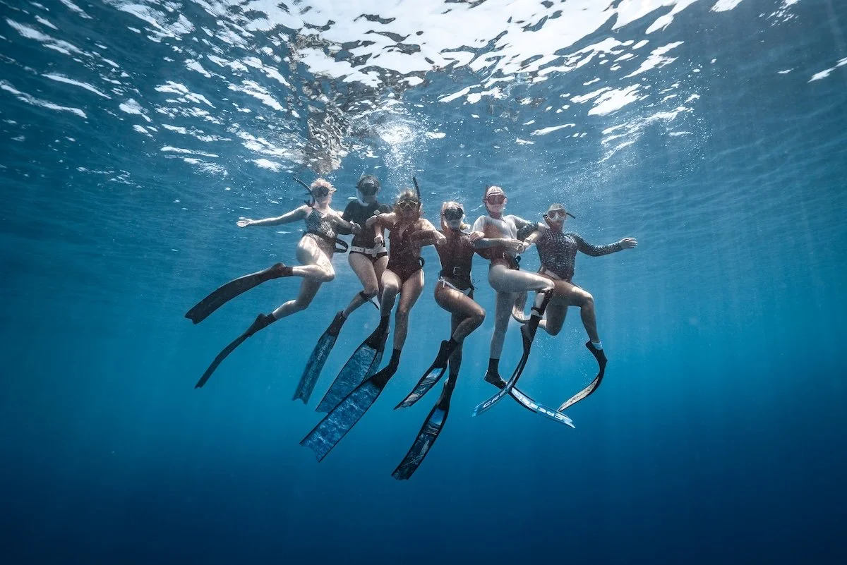Group of 6 freedive girls linking arms underwater