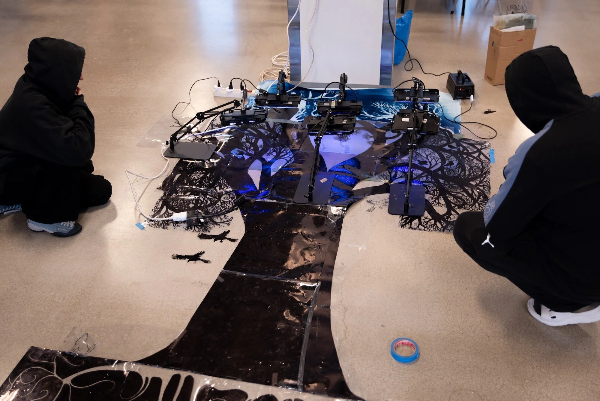 Sceneteppe til Ringerike fengsel, avdeling Ullersmo, i samarbeid med en gruppe innsatte. Teknikk og materiale: Cyanotype på tekstilbiter i bomull, lin, silke og ull, broderi i ull, silke og bomull, applikert på kraftig bomullstekstil. Håndsøm. Fôret 