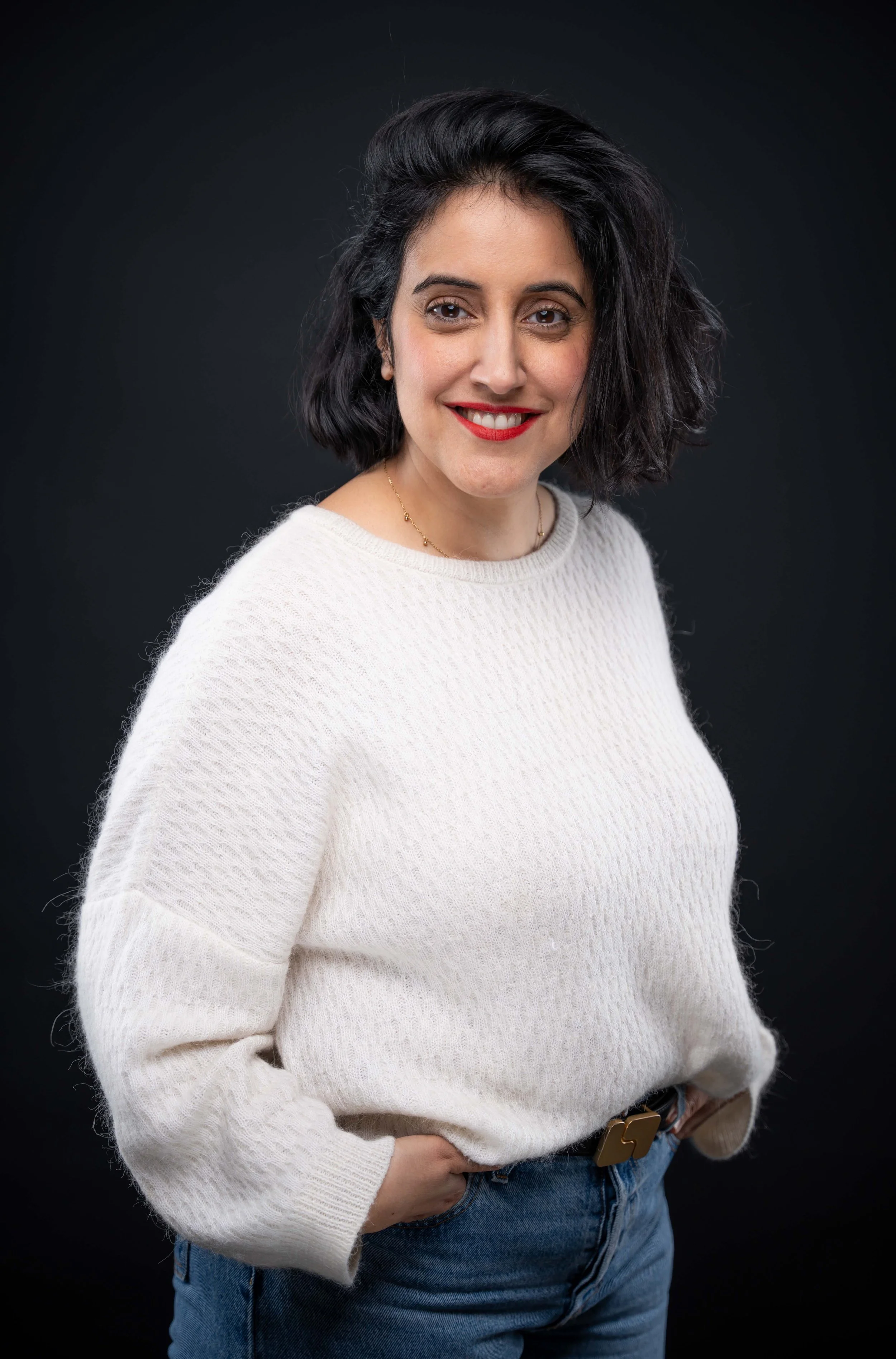 Femme souriante portant un pull blanc et un jean, avec un fond noir