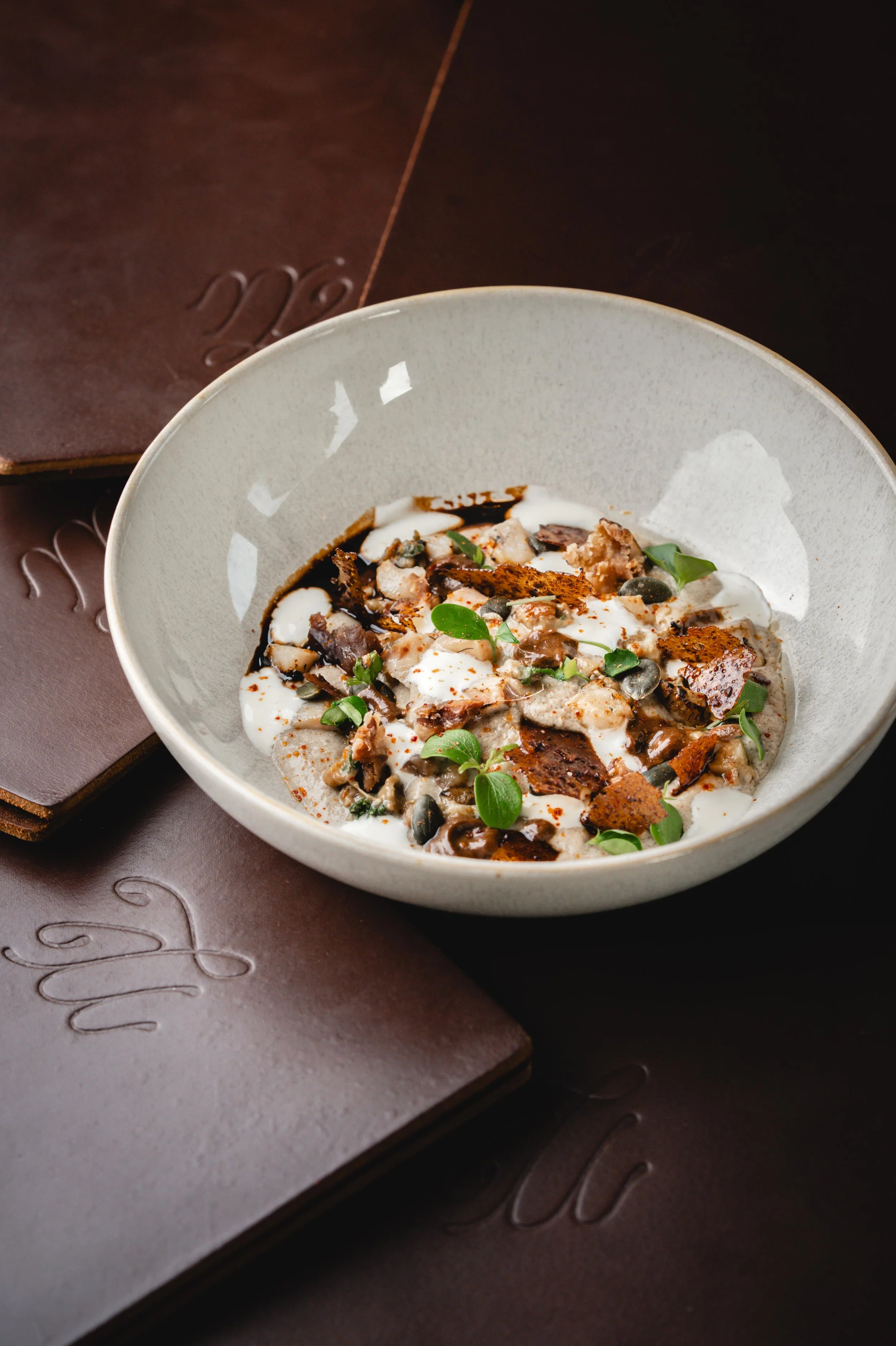 Une assiette de dessert avec de la crème, des morceaux de chocolat, des graines et des feuilles vertes, accompagnée de morceaux de chocolat sur le côté, sur un fond sombre.