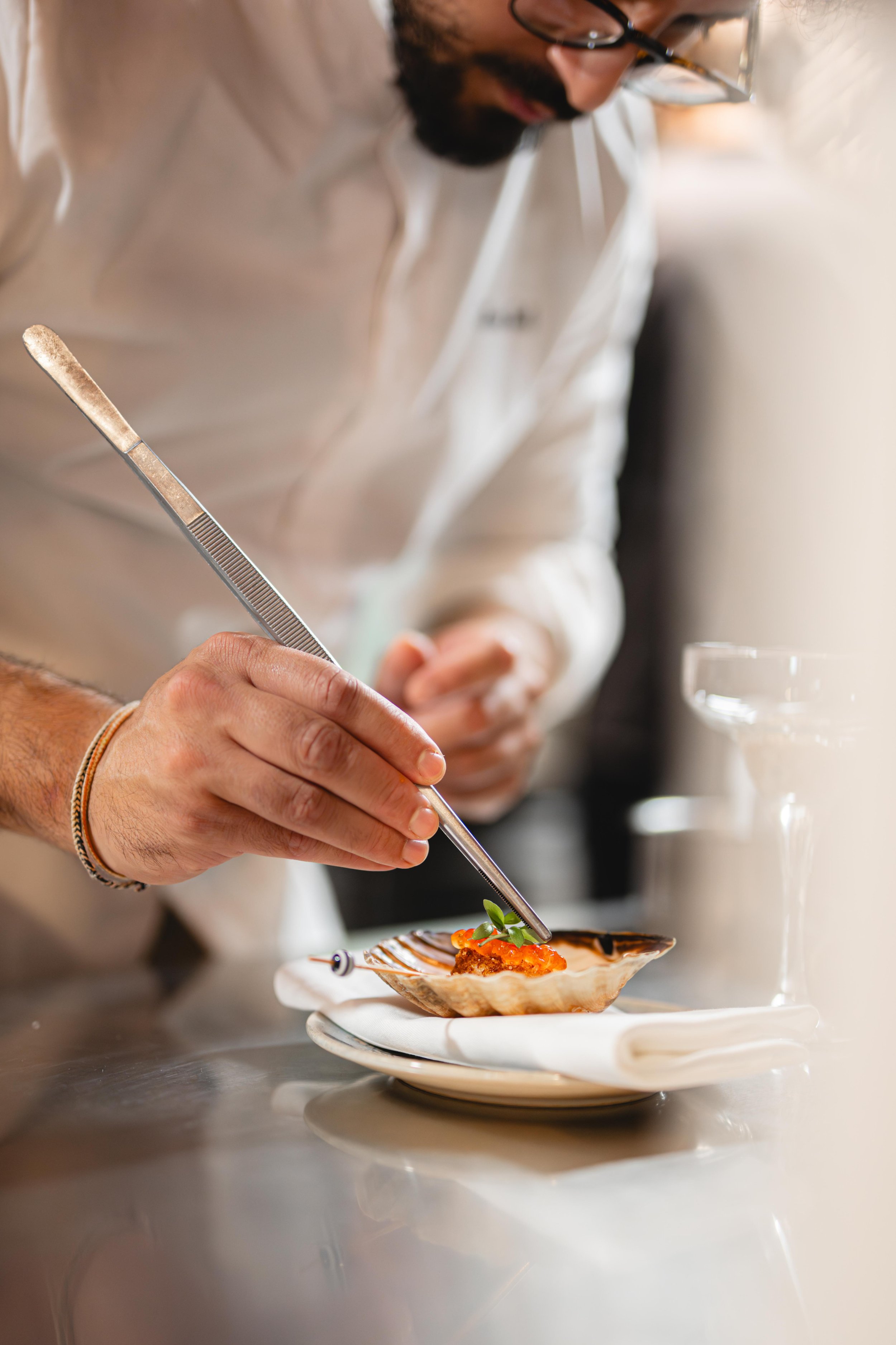 Un chef cuisine un plat sophistiqué avec des pinces dans une cuisine professionnelle