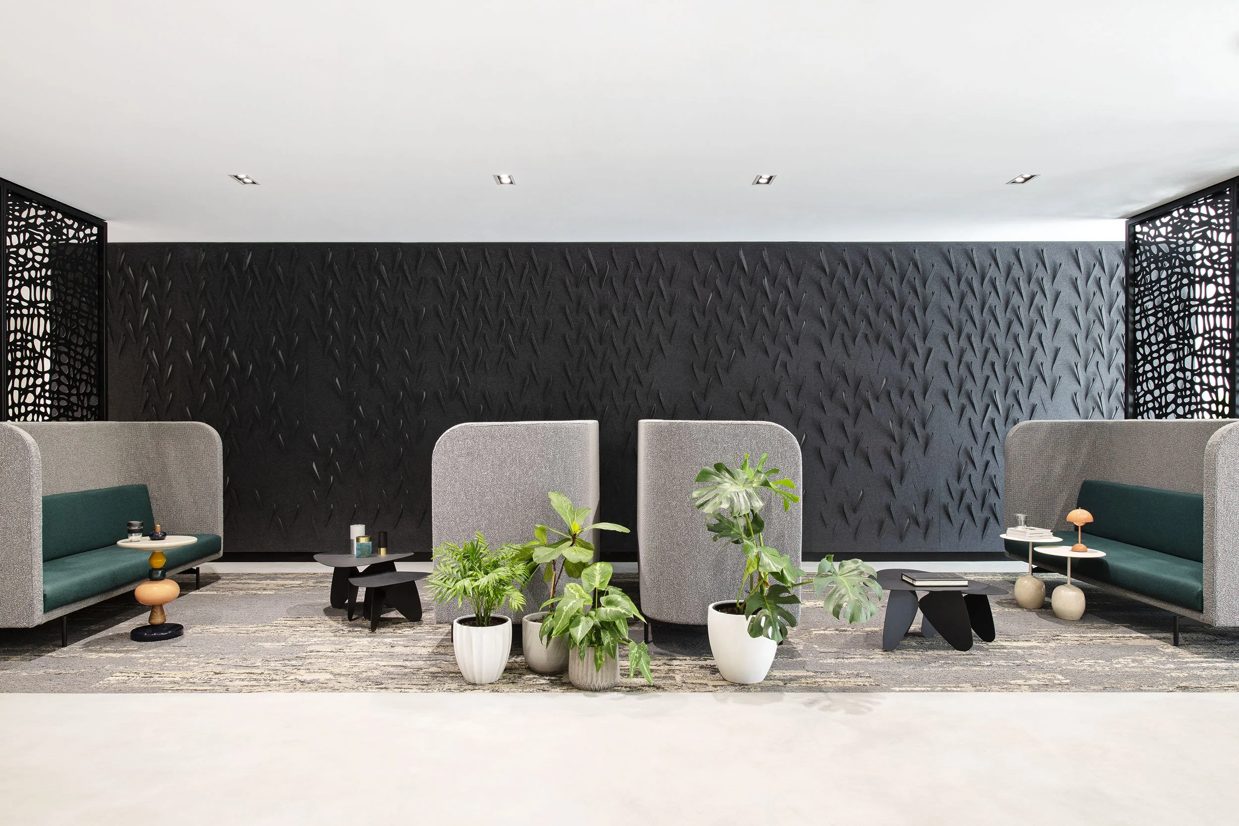 Modern lobby with black textured wall, gray seating with green cushions, and indoor plants in white pots.