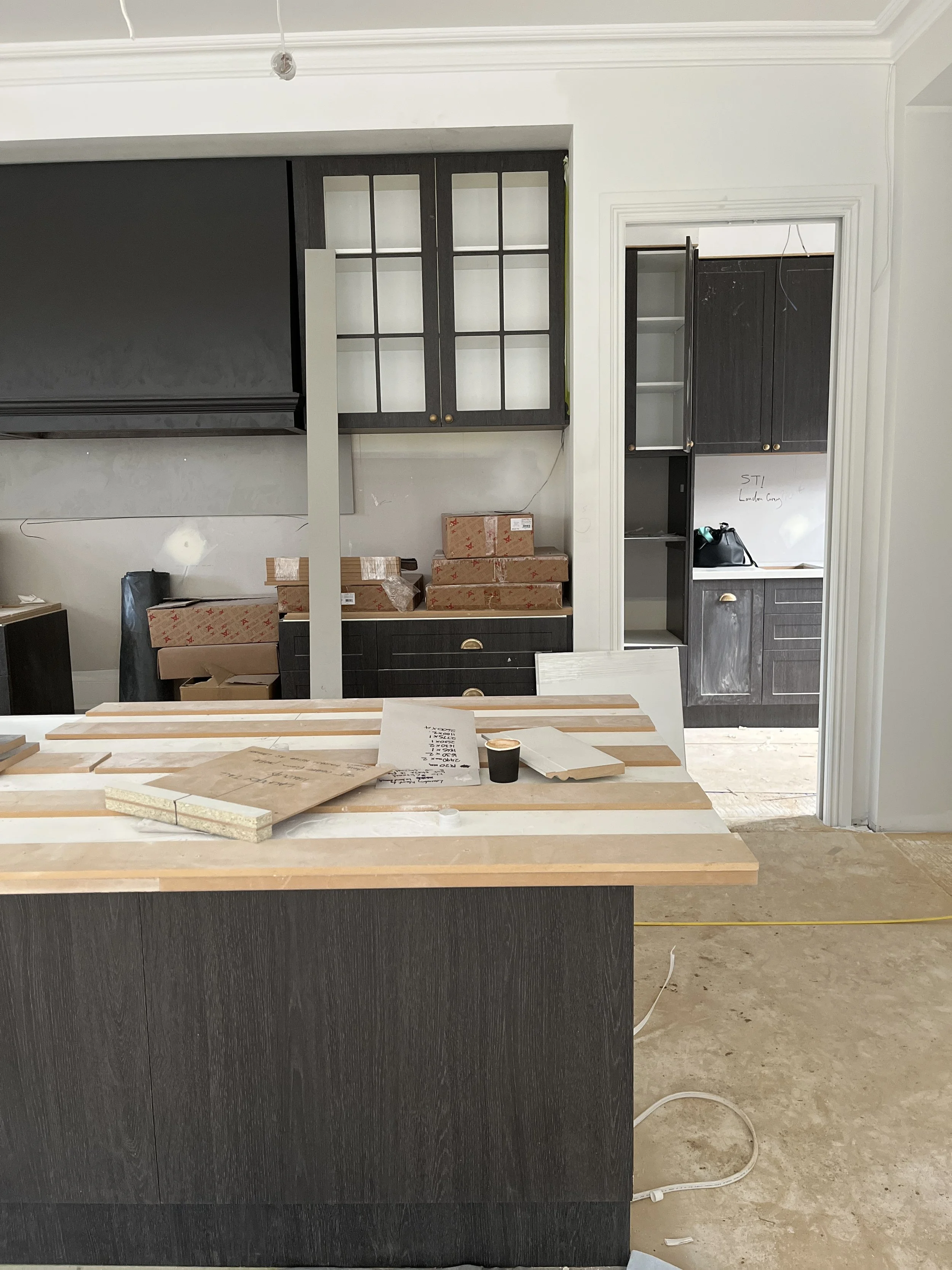 Kitchen undergoing renovation with unfinished countertops, cabinets, and various construction materials on the island.