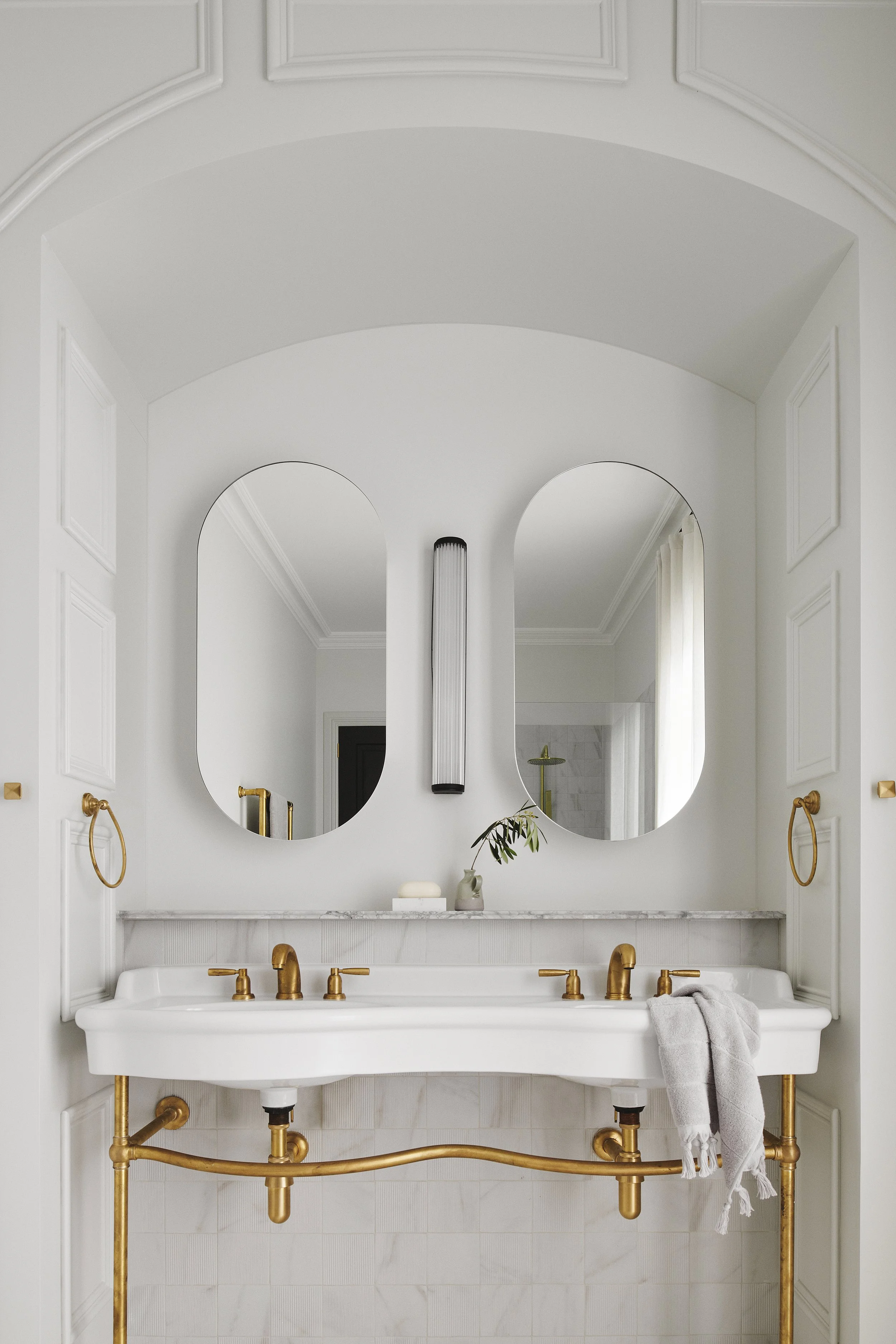 A modern white bathroom vanity with gold fixtures, a large mirror, and a small decorative plant on the countertop.
