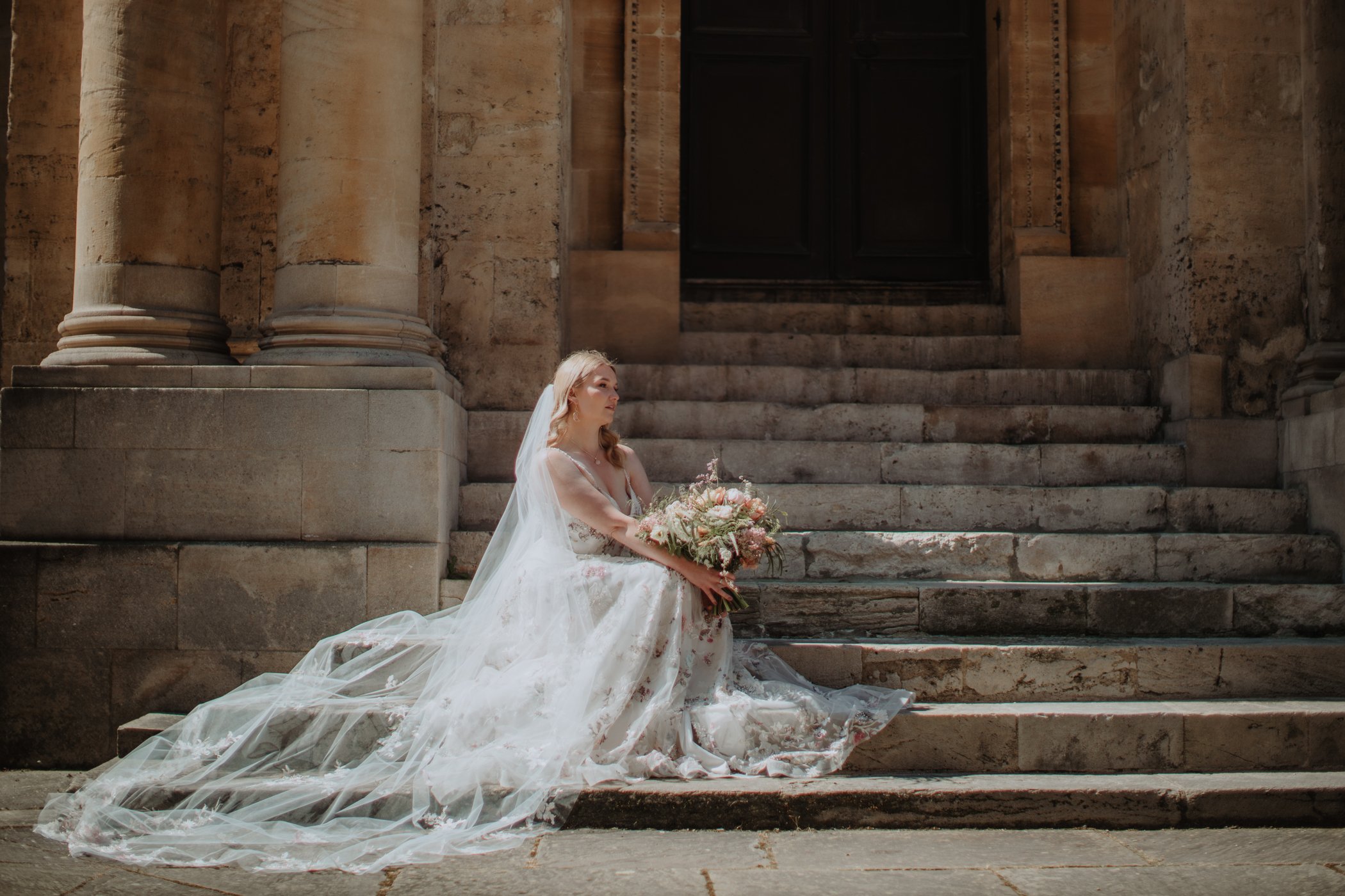 Bride is floral bridal gown sitting on steps