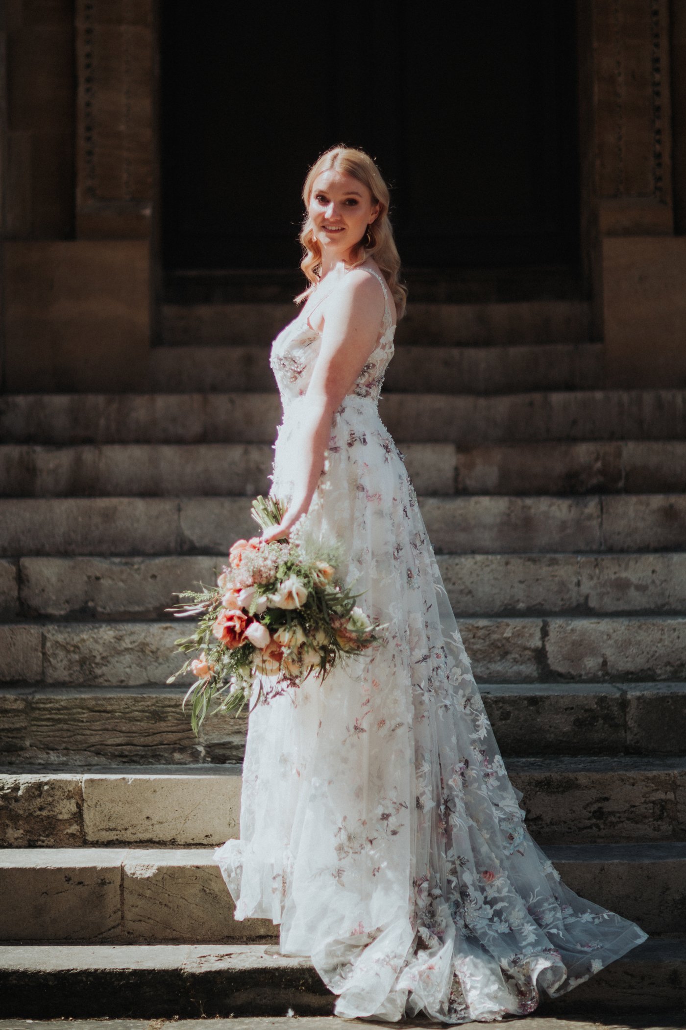 Bride in floral dress with bouquet on steps of Bodleian Libraryn