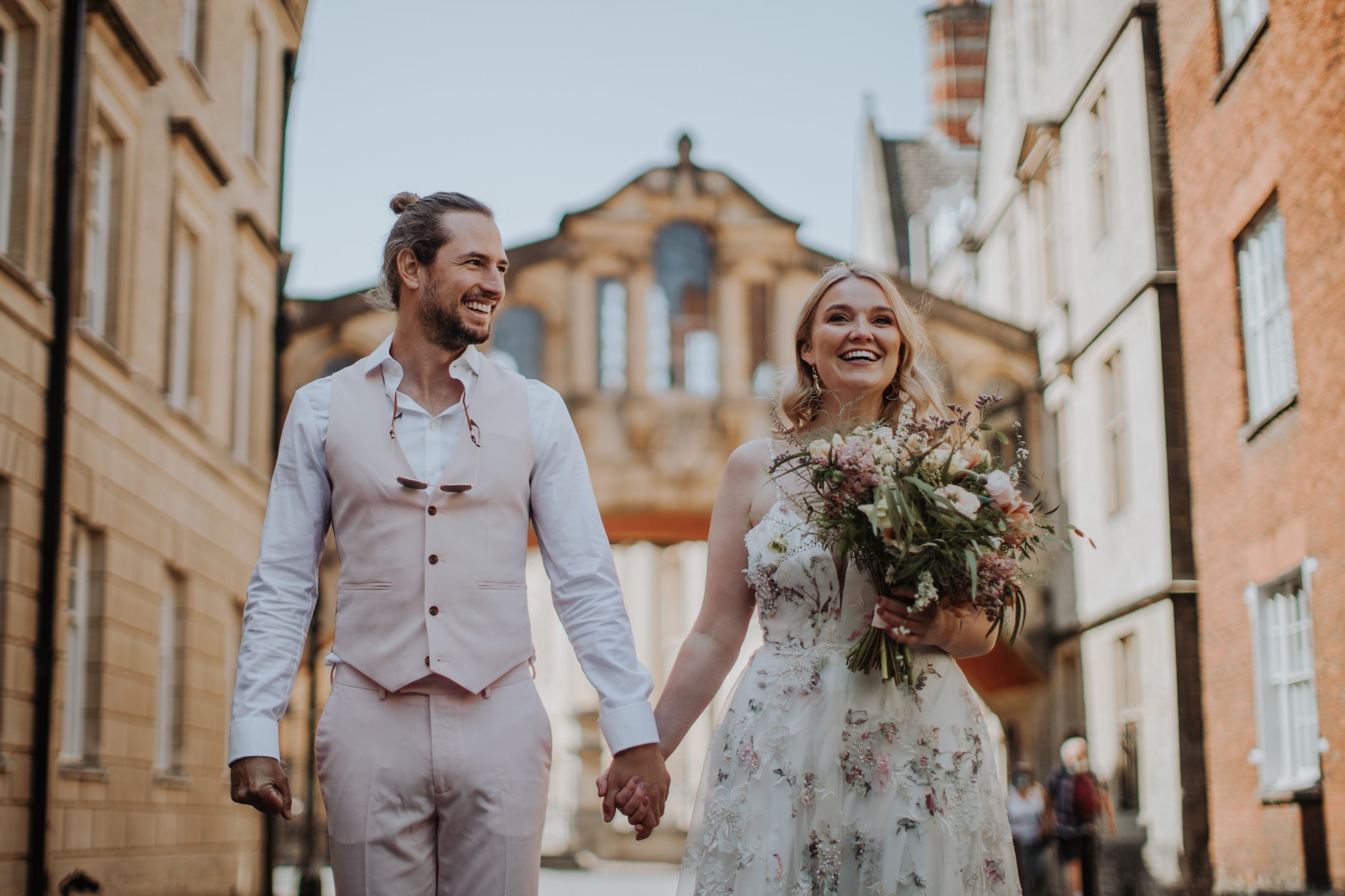 Bride and groom holding hands laughing under Bridge of Sighs Oxford