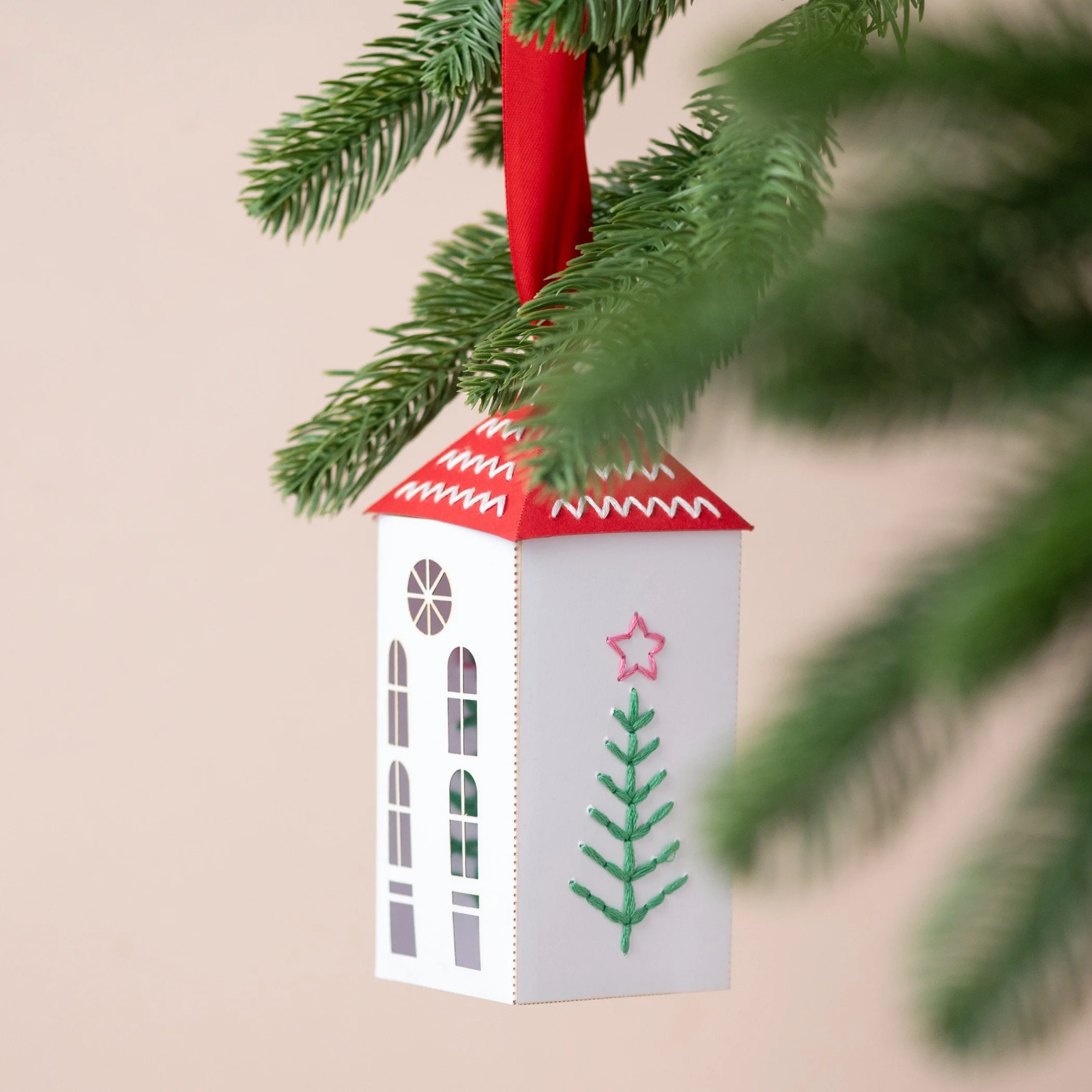 a embroidered paper house , by My Papercut Forest, hanging from a Christmas tree
