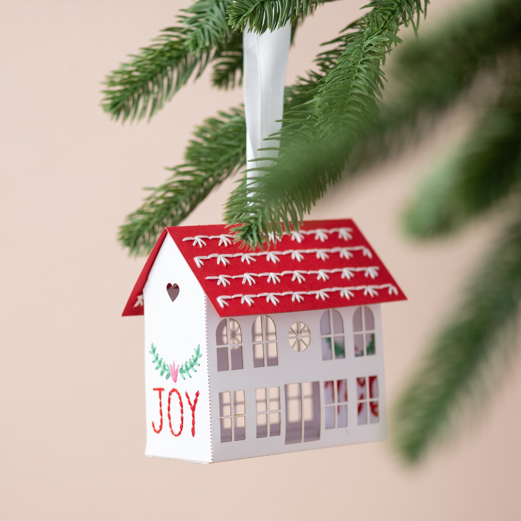 a embroidered paper house , by My Papercut Forest, hanging from a Christmas tree