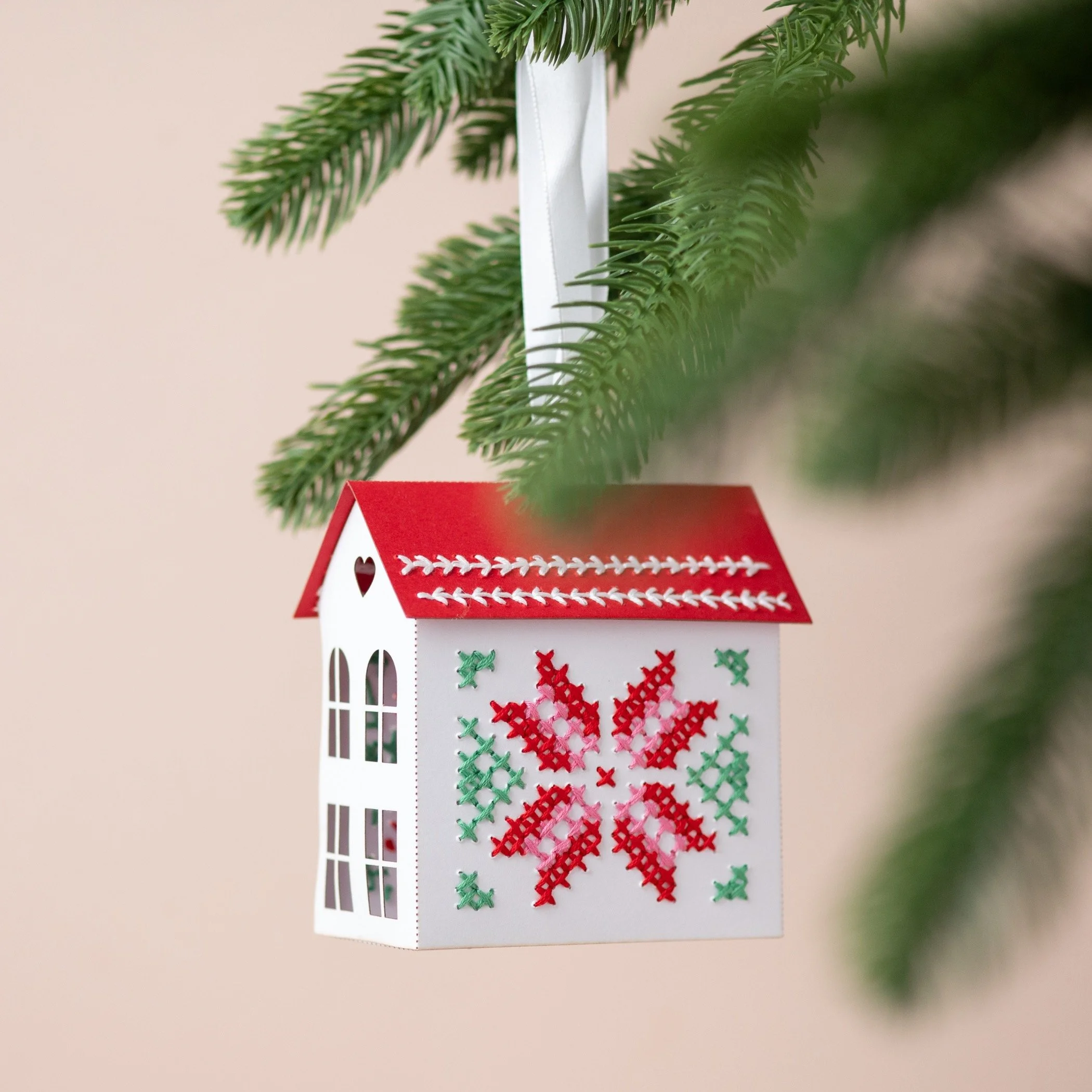 a embroidered paper house , by My Papercut Forest, hanging from a Christmas tree