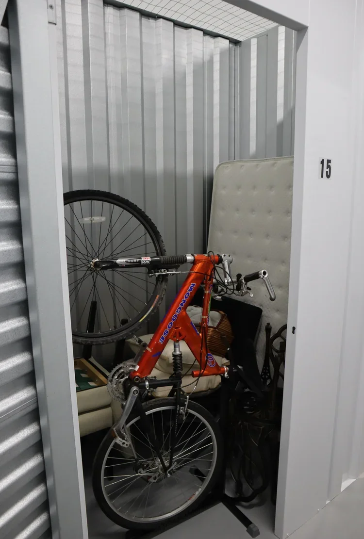Storage unit containing an orange mountain bike, a white foam pad, and various bags.