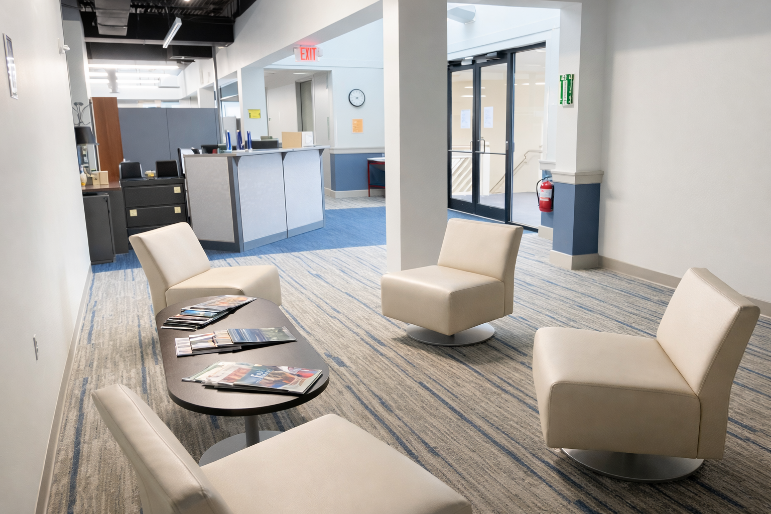 Bright second-floor waiting area with four cream lounge chairs around a low coffee table with magazines, next to a reception desk and glass entry doors.