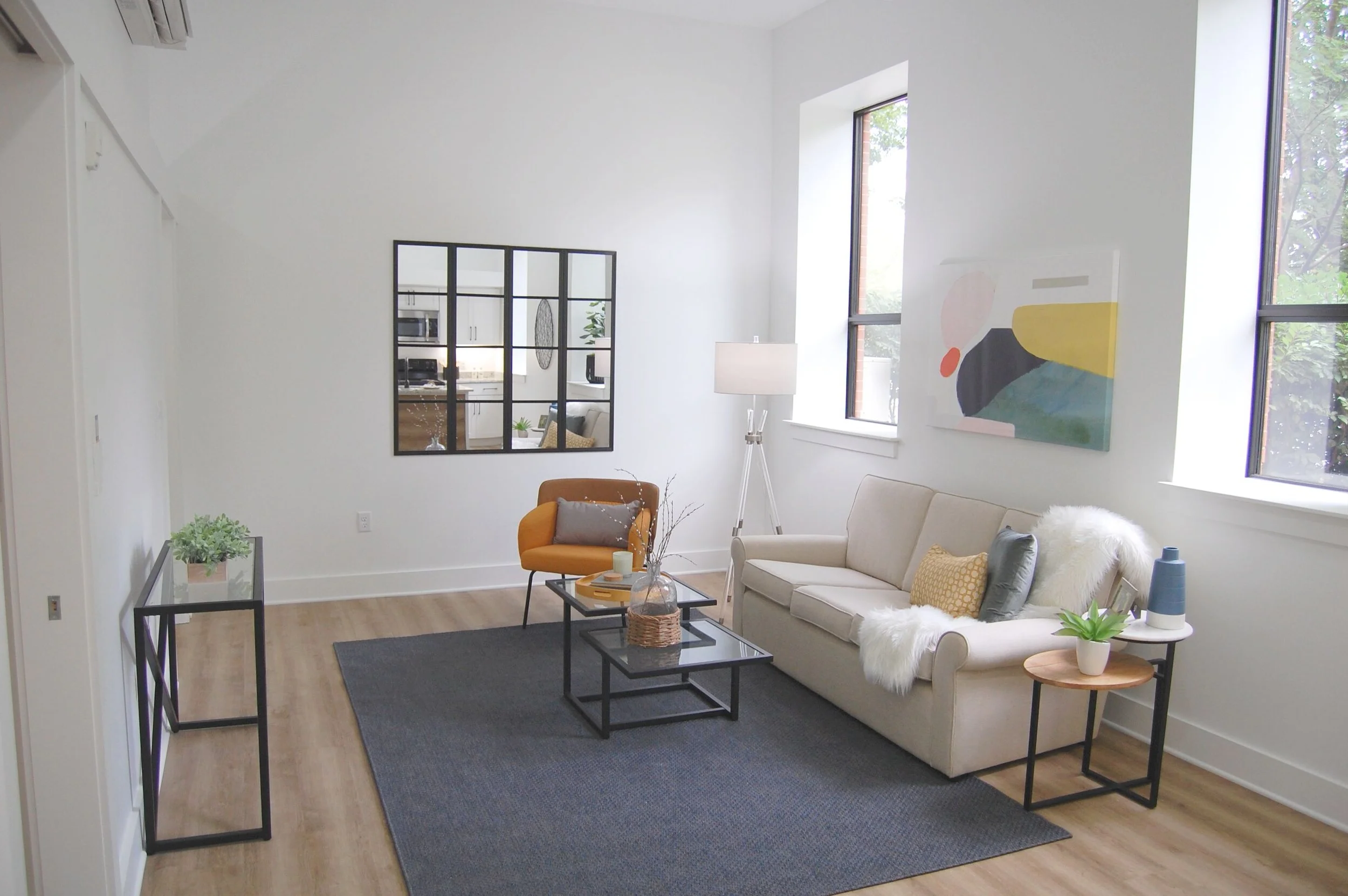 Modern living room with cream sofa, yellow chair, black coffee tables, and large windows, decorated with abstract art and plants.