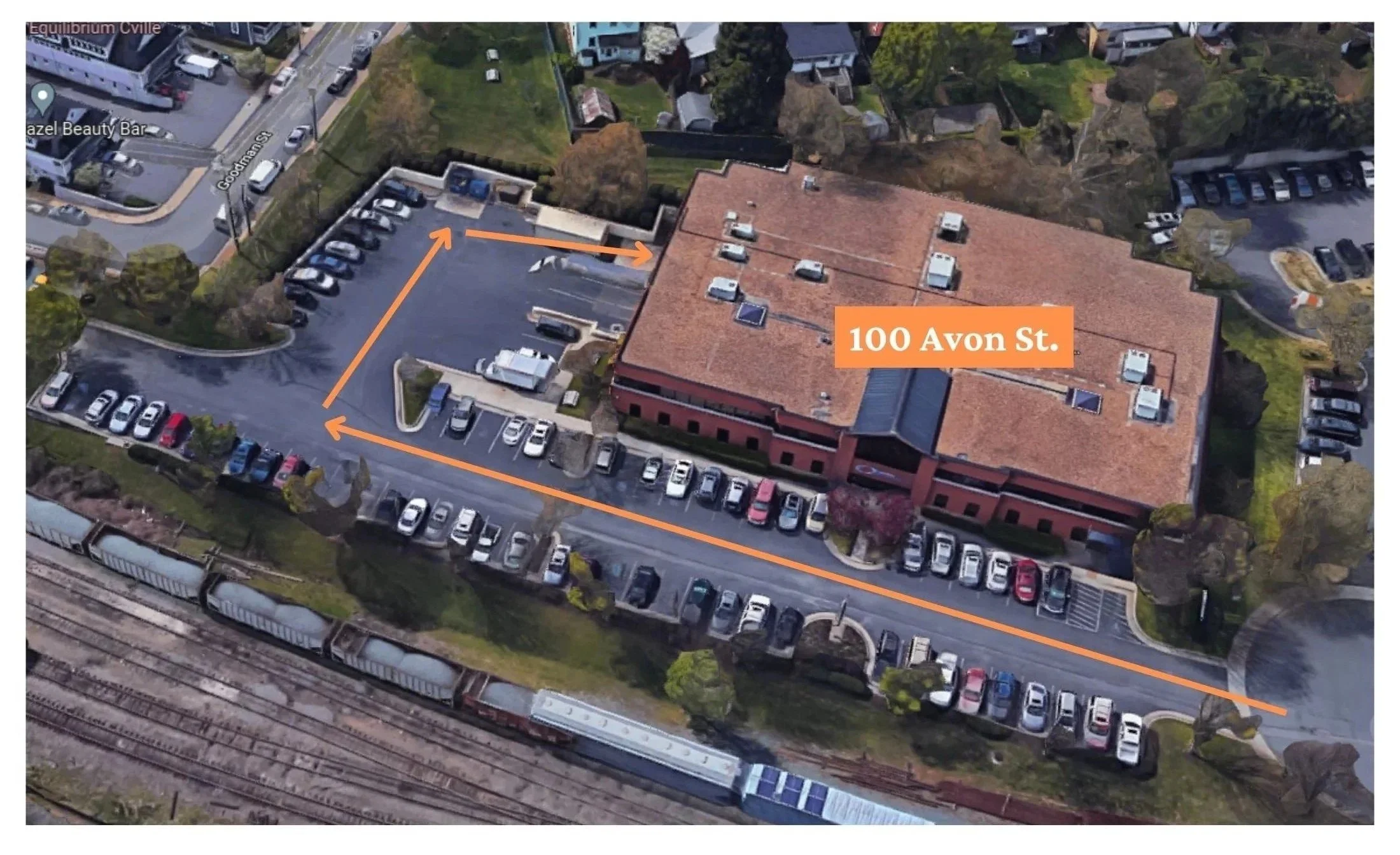 Aerial view of a parking lot and building at 100 Avon St., with orange arrows indicating a driving route around the lot to get to the loading area for the storage units.