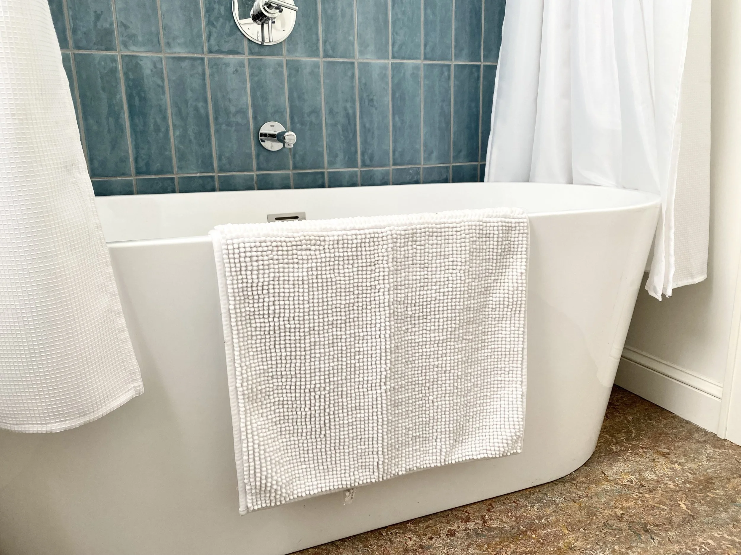 White bathtub with a textured towel draped over the side, against a background of blue tiled wall and white shower curtain.