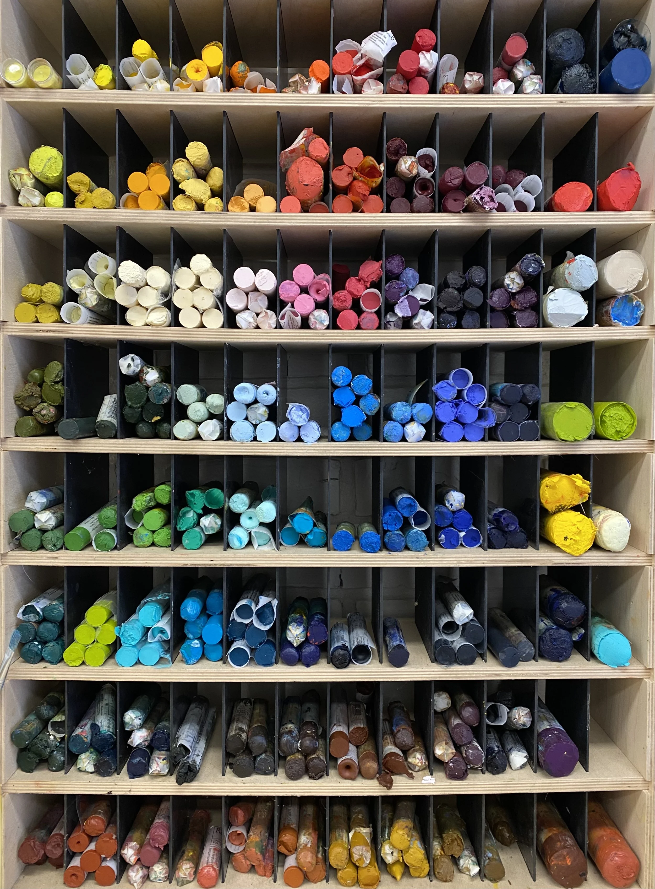 Assorted Pigment Sticks organized in a wooden storage rack with individual slots.