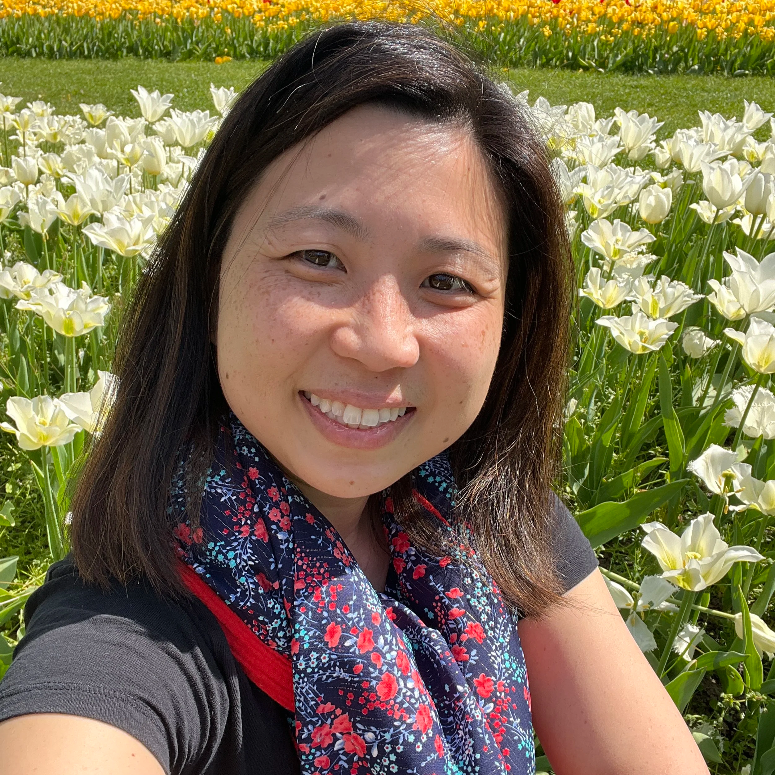 Grief doula Christine Nguyen, smiling in a field of wildflowers near Paris, offering compassionate virtual grief support in France.