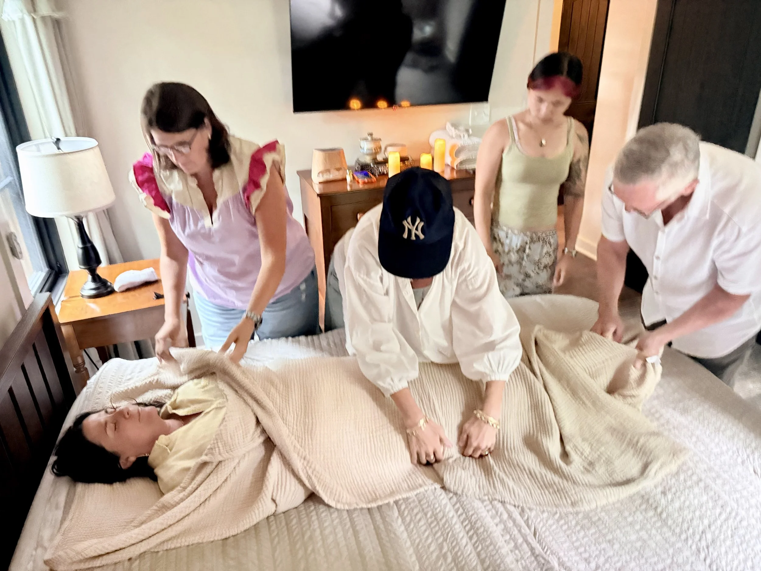 Advanced death doula training students practicing burial shrouding techniques during an in-person retreat, learning hands-on after-death care practices and compassionate end-of-life support.