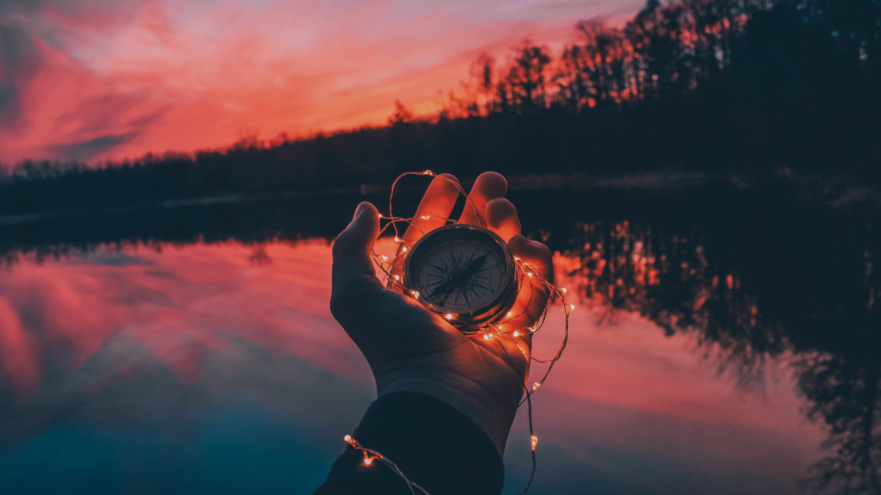 Hand holding a compass with fairy lights at sunset, symbolizing guiding families through advance care planning, end-of-life conversations, and meaningful legacy projects.