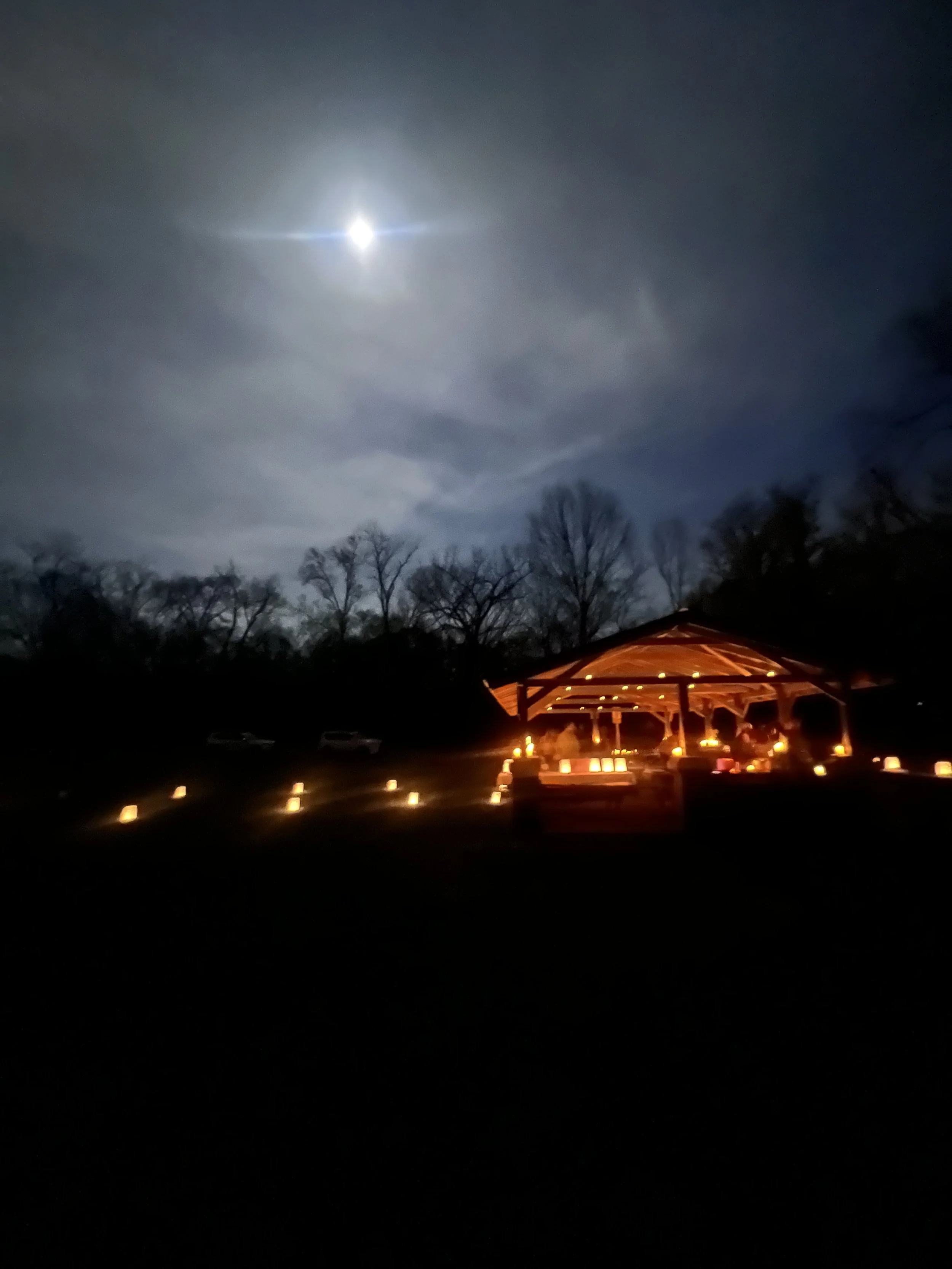 Farewell Doulas and apprentices facilitating a community grief circle at a park shelter under the moonlight, lit by candles, in Nashville Tennessee.