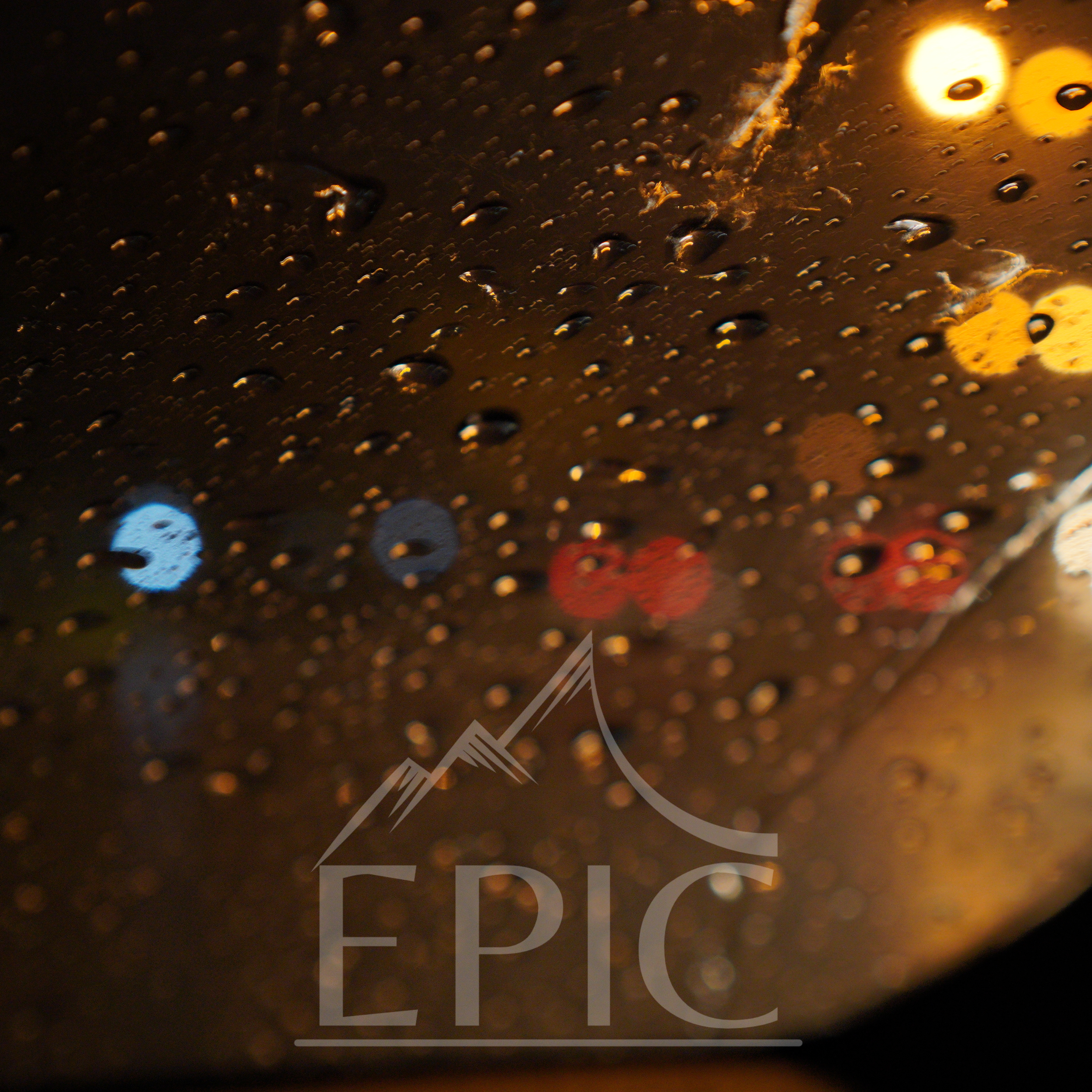 Close-up of a wet surface with raindrops, showing blurred colorful lights in the background at night.