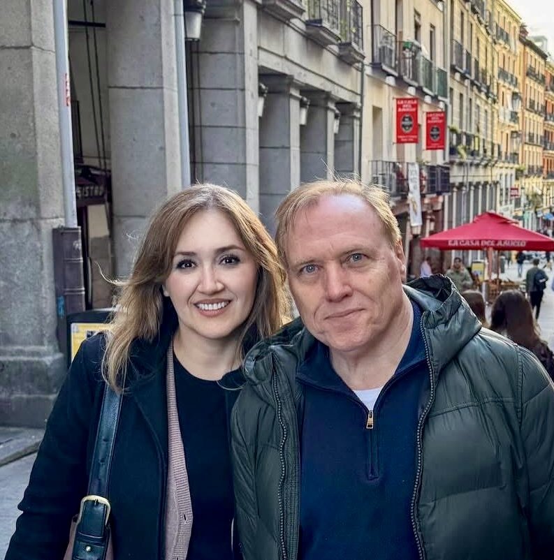 Una mujer y un hombre sonriendo en una calle de la ciudad, con edificios coloridos al fondo.
