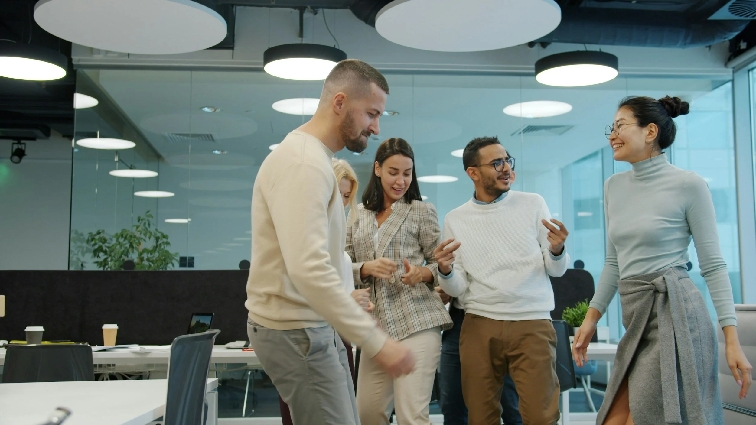 Five coworkers laughing and talking together in a bright open office.
