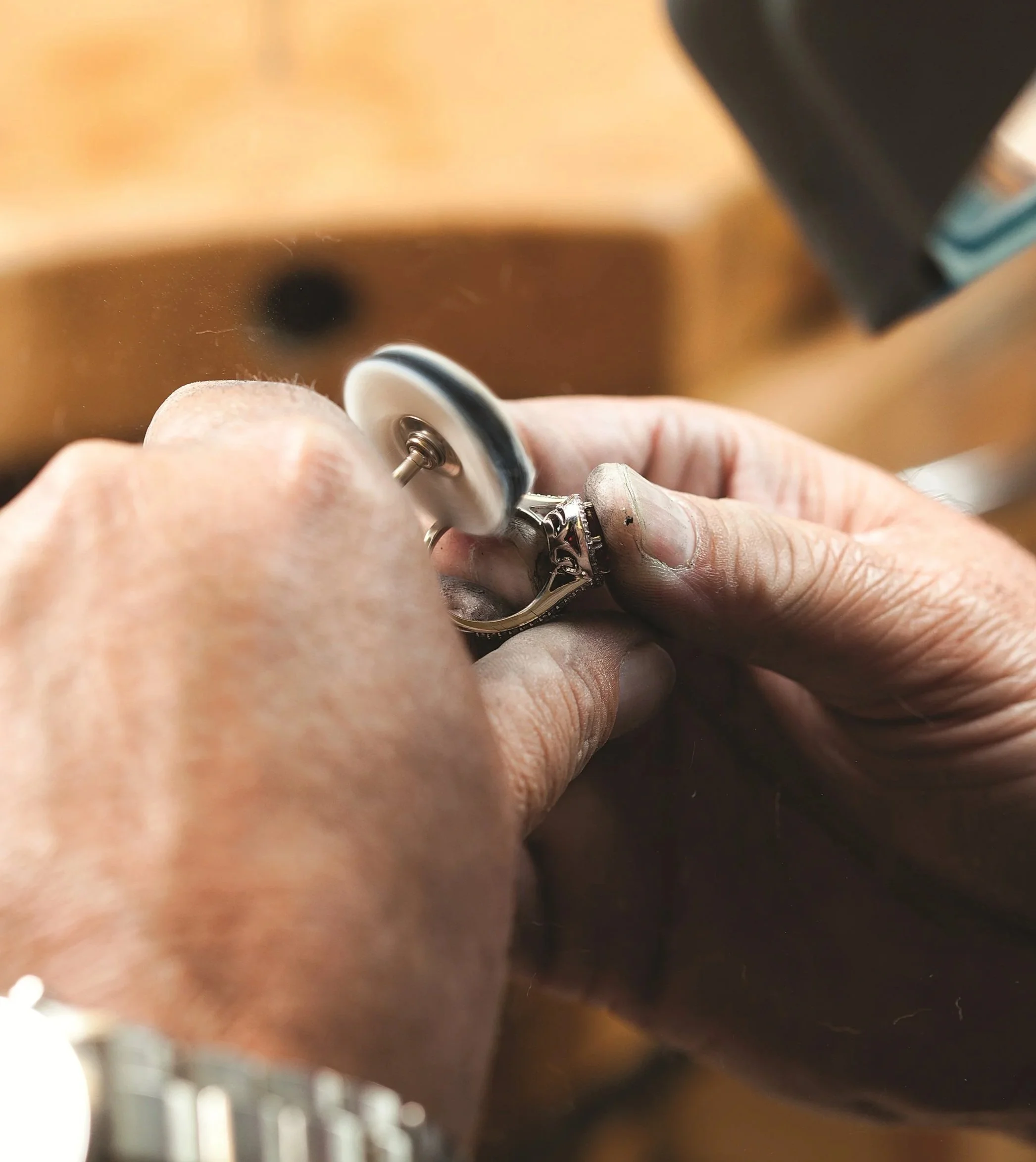 Close-up of a person's hands polishing a silver ring with an electric rotary tool in a jewelry workshop.