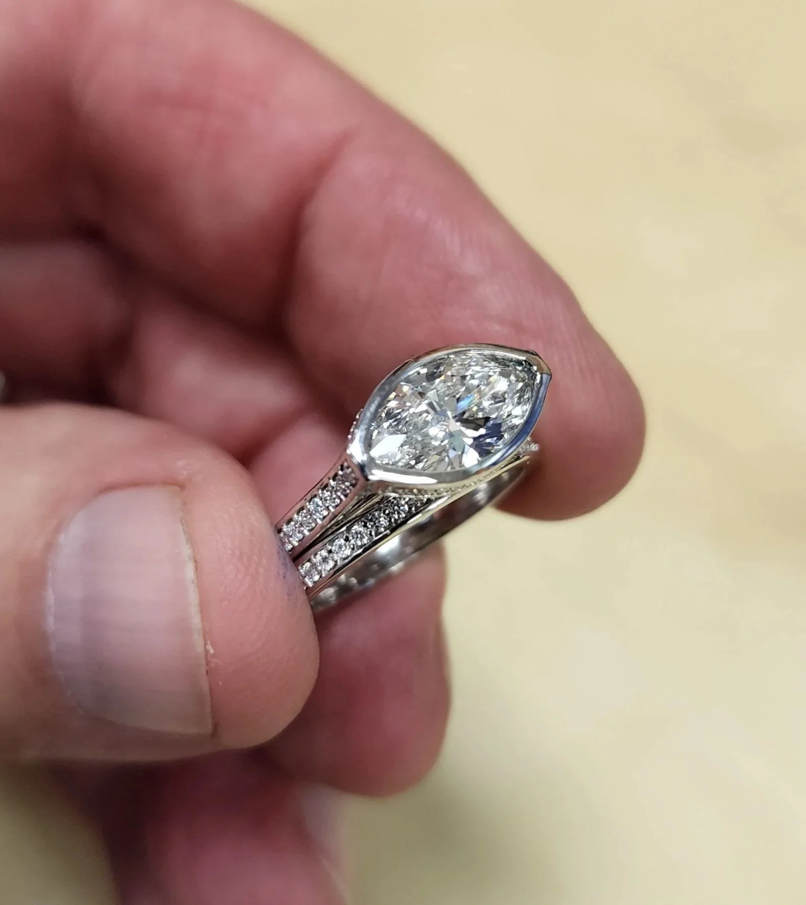 Close-up of a hand holding a diamond engagement ring with a marquise-shaped diamond and smaller diamonds on the band.