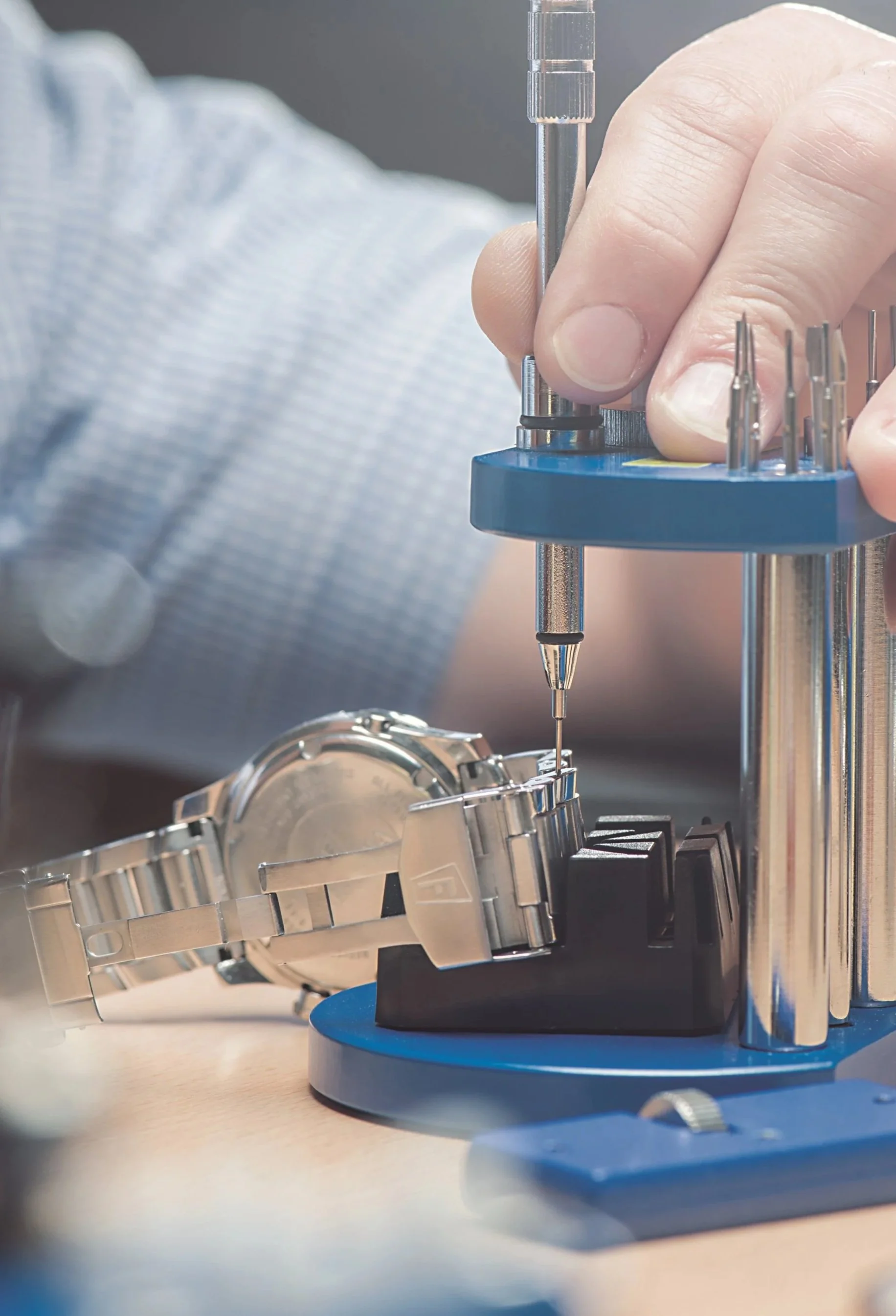 A watchmaker repairing a wristwatch using precision tools and a specialized watch repair station.