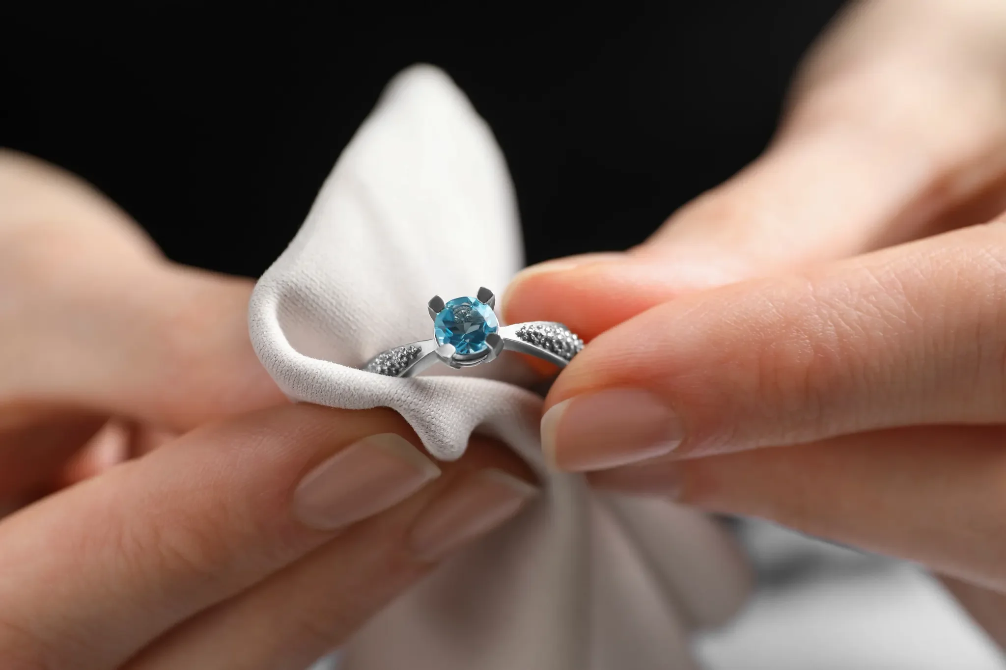 Close-up of a hand holding a ring with a blue gemstone, wrapped in a white cloth or glove.