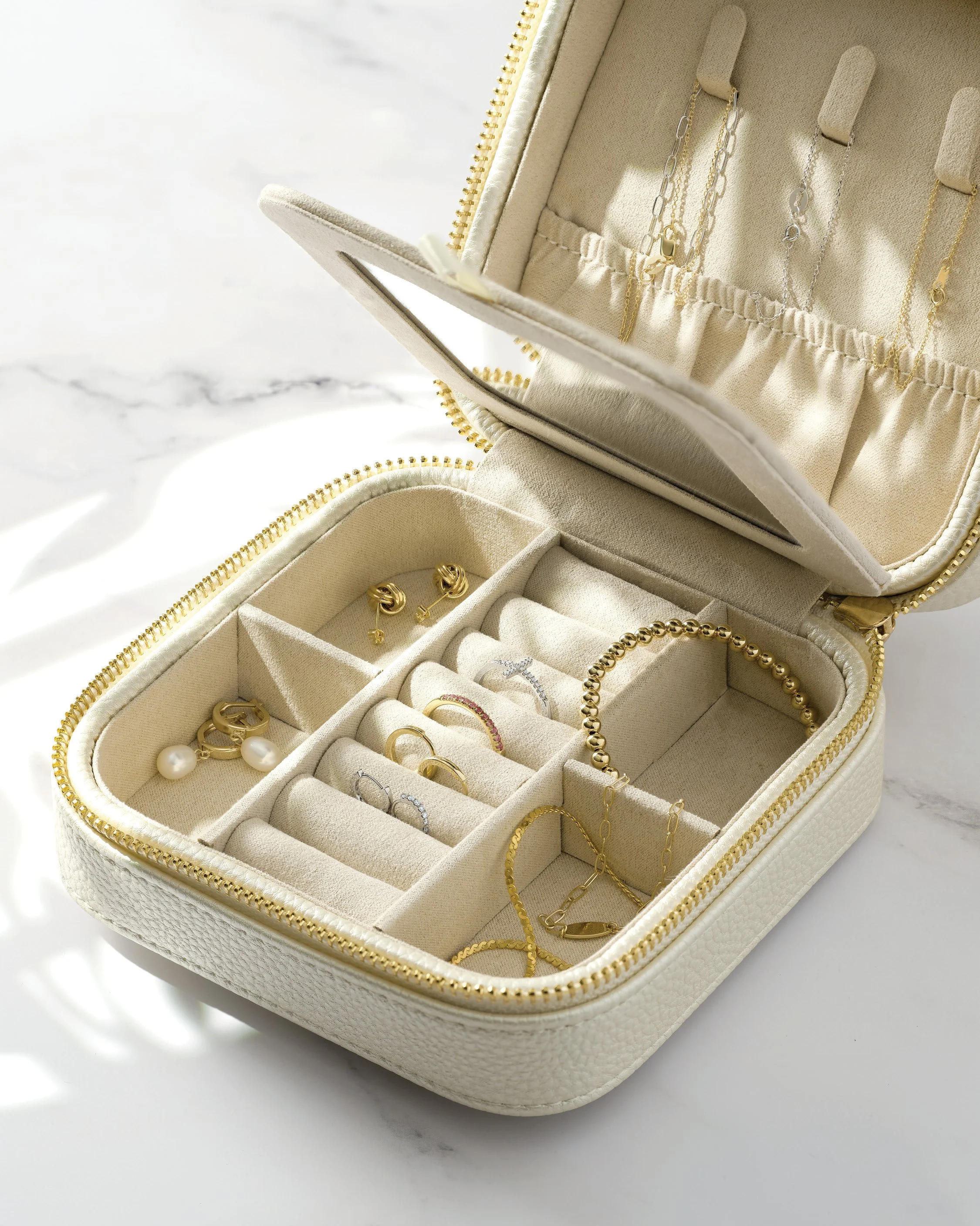 Open jewelry box with rings, earrings, necklaces, and bracelets inside, on a white marble surface.