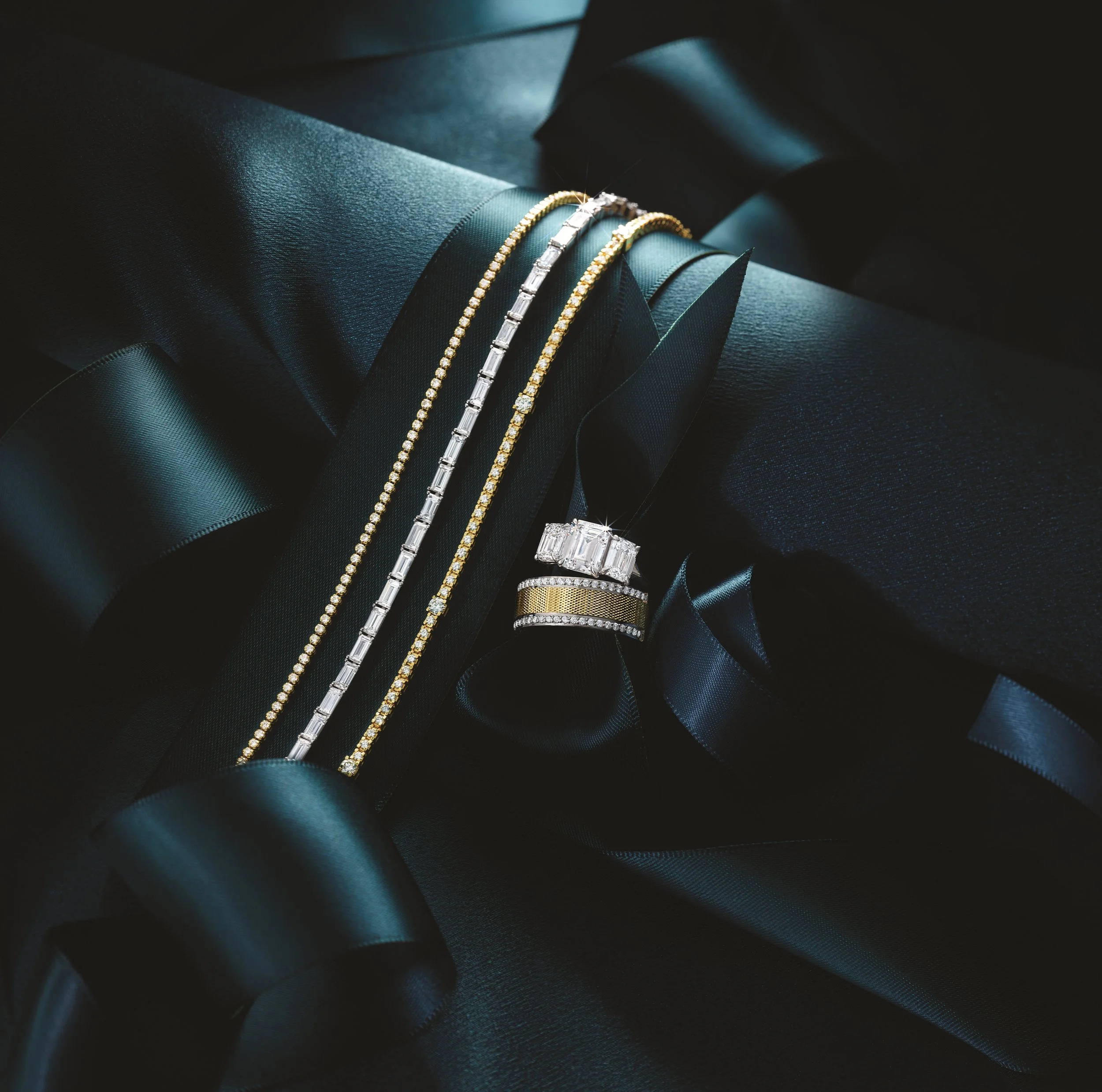 A collection of gold and silver jewelry including necklaces, rings, and bracelets, displayed on black satin ribbon and a black gift box.