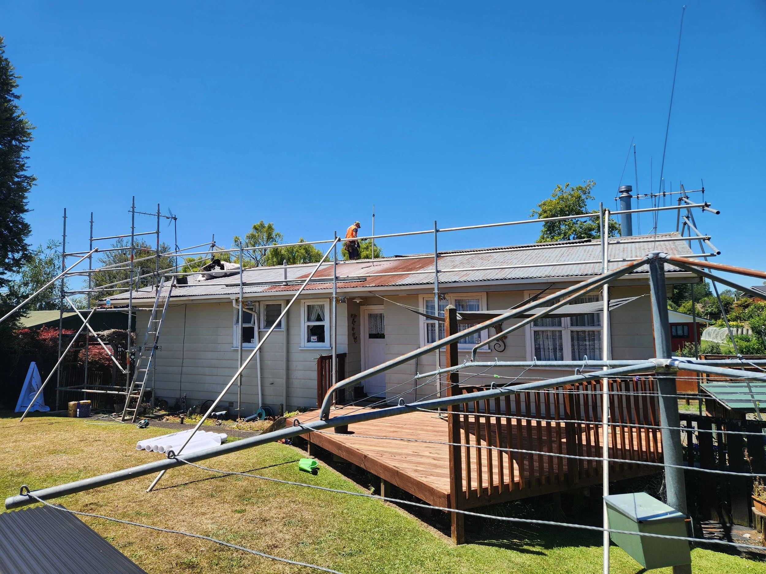 A person working on a house roof surrounded by scaffolding on a sunny day.