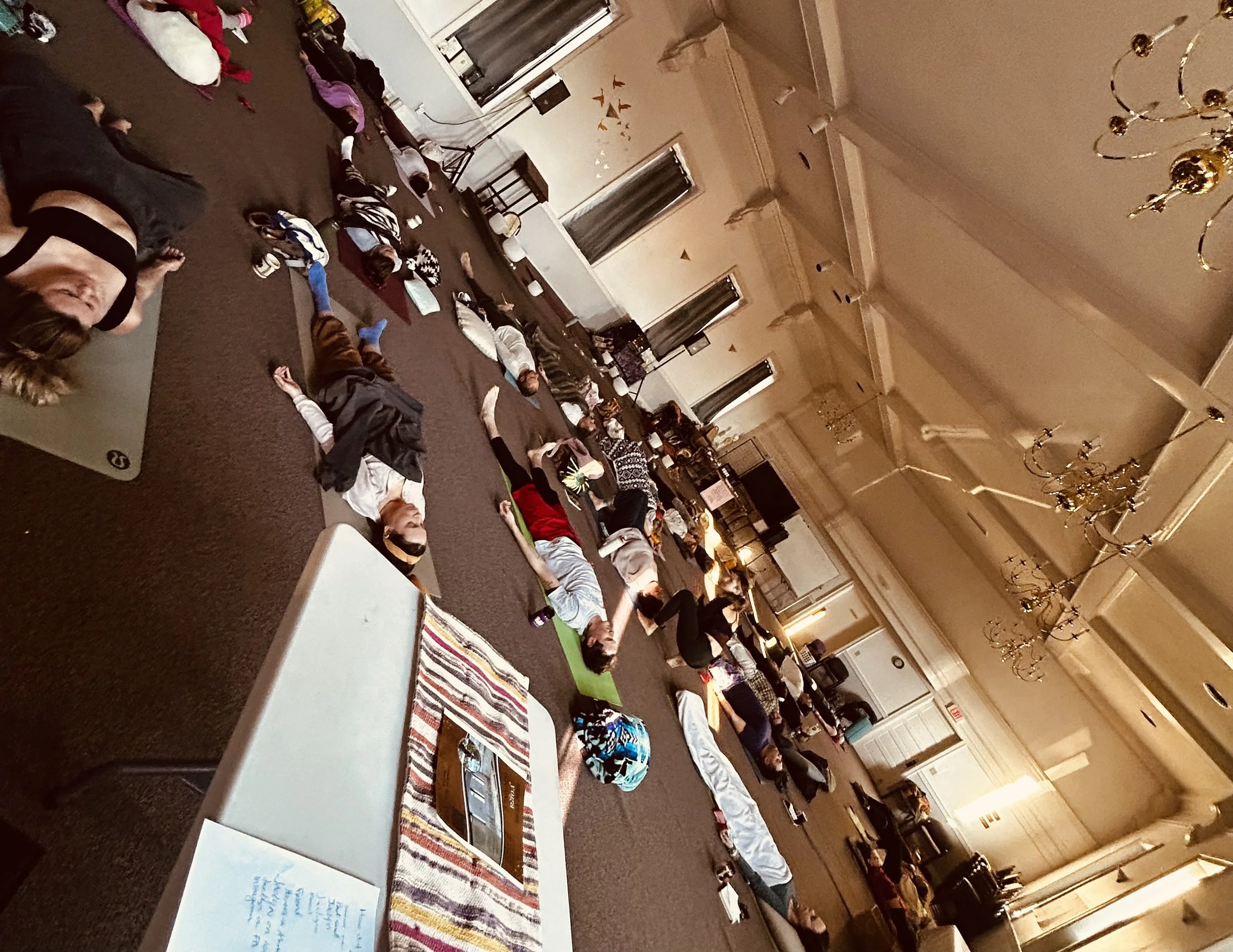 Community Sound Healing Session Omaha, NE. People lying on yoga mats in a large, ornate room participating in a group yoga or meditation session.