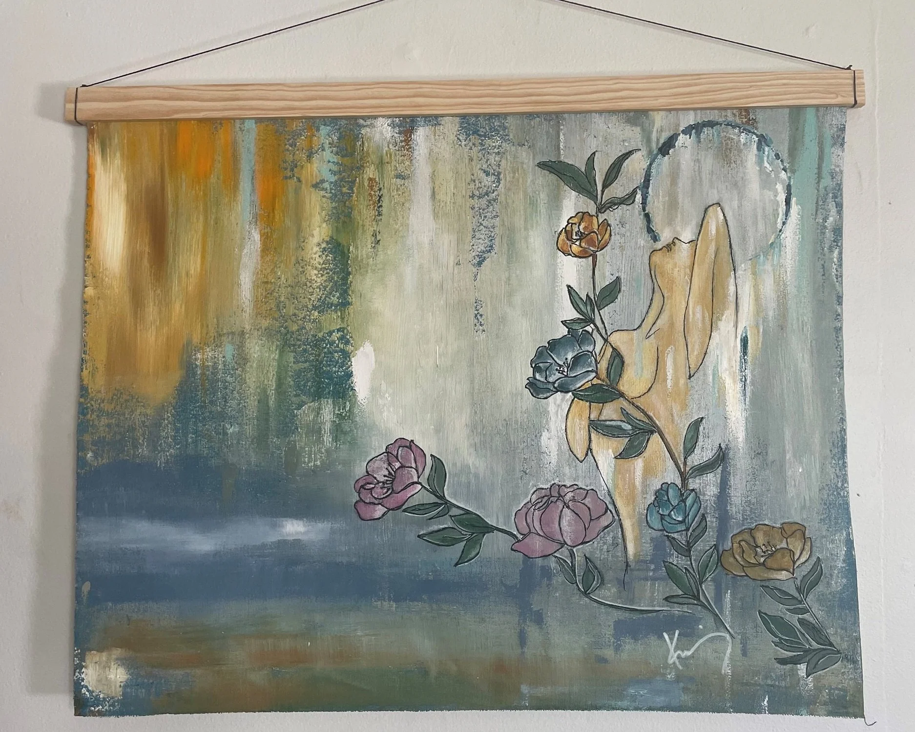A decorative wall hanging featuring a painted scene with abstracted nature elements and outlined flowers in pink, purple, yellow, and blue, with a landscape background in muted colors, mounted on a wooden rod with a hanging string.