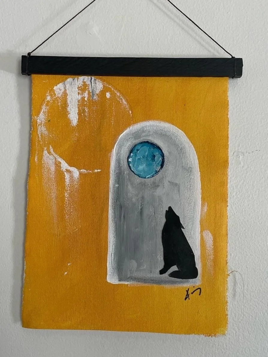 Painting on yellow fabric featuring a moonlit scene with a black silhouette of a sitting wolf or dog inside a small arched window, with a textured blue circular moon outside the window.