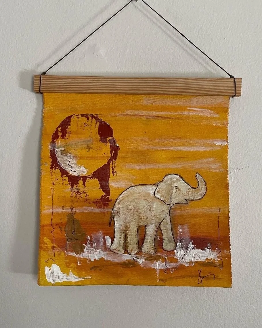 Painted wall hanging with an elephant and a stylized portrait of a woman against an orange background.