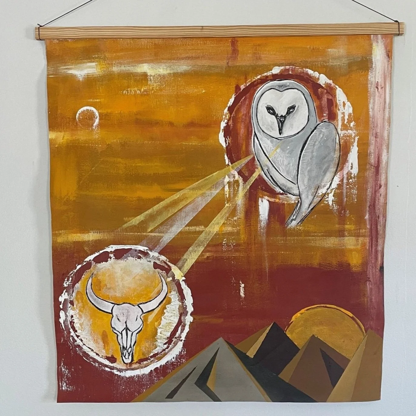 A painting with a Western desert scene featuring mountains, a yellow sky, and two large circular images of animals: an owl above and a buffalo skull below, both within circular borders.