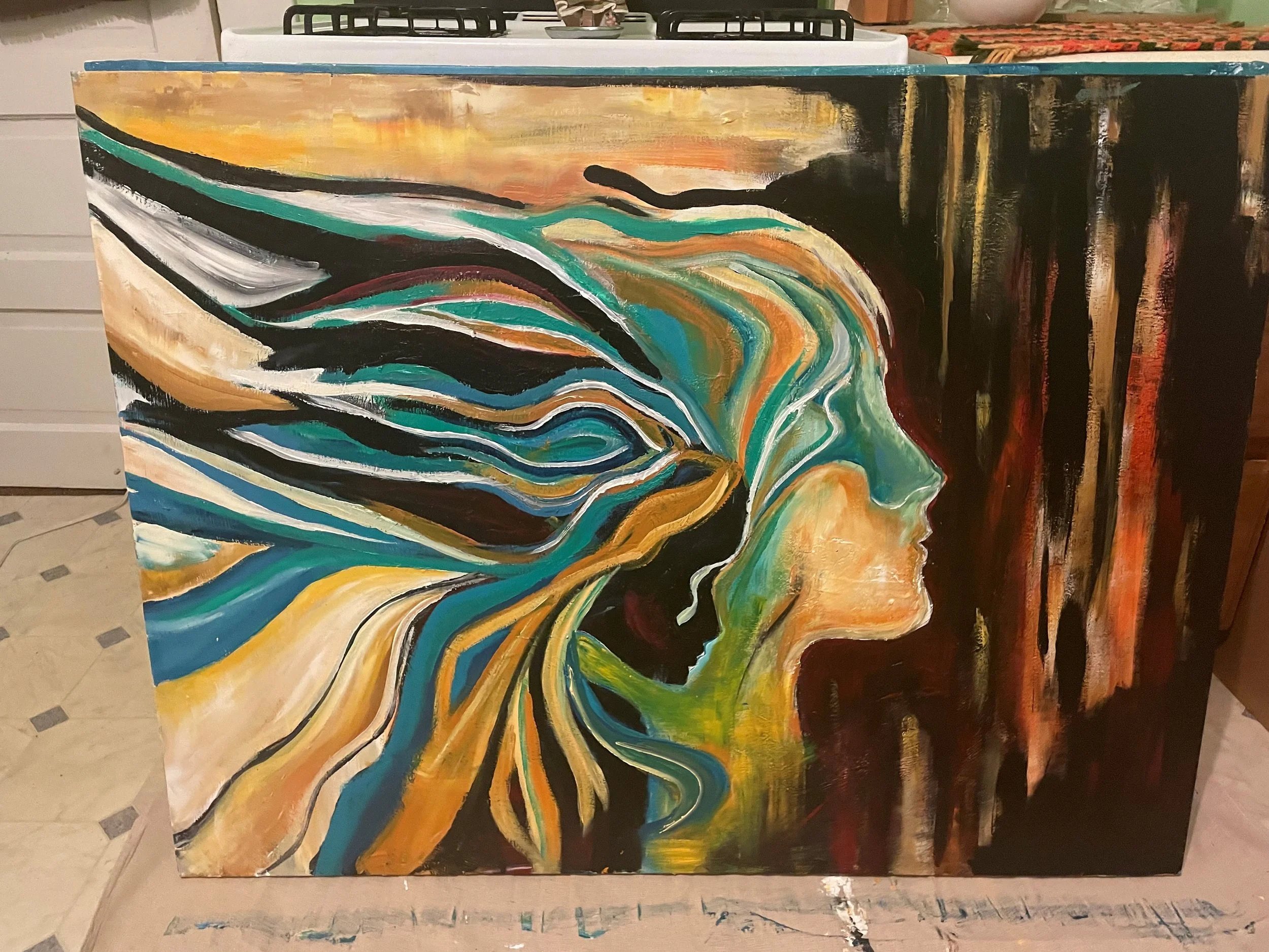 A colorful abstract painting featuring swirling patterns of blue, green, yellow, black, and white on a rectangular canvas leaning against a white surface in a room.