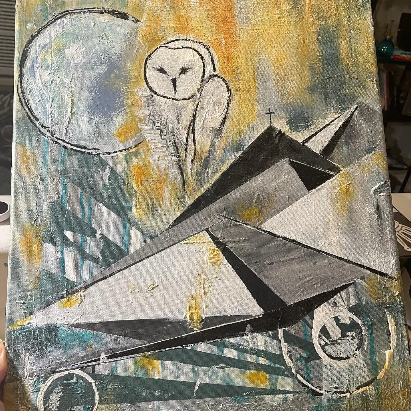 A painting featuring a white owl with black outlines perched on a rooftop with a cross, a large moon in the sky, and abstract geometric shapes and colors in the background.