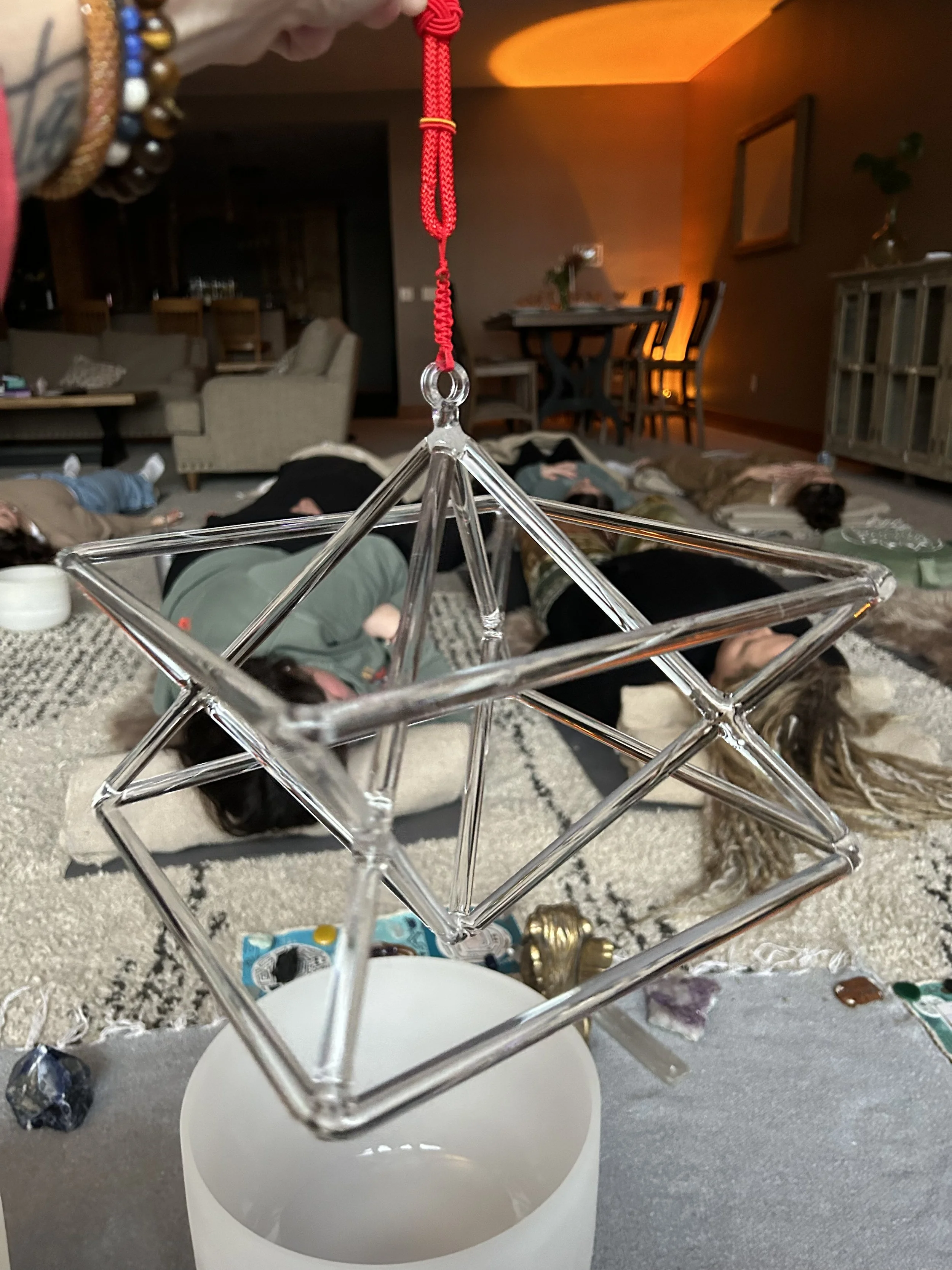 Sound Healing inOmaha, NE. A person hanging a red cord with a metal clasp onto a small, clear, geometric wireframe display stand.